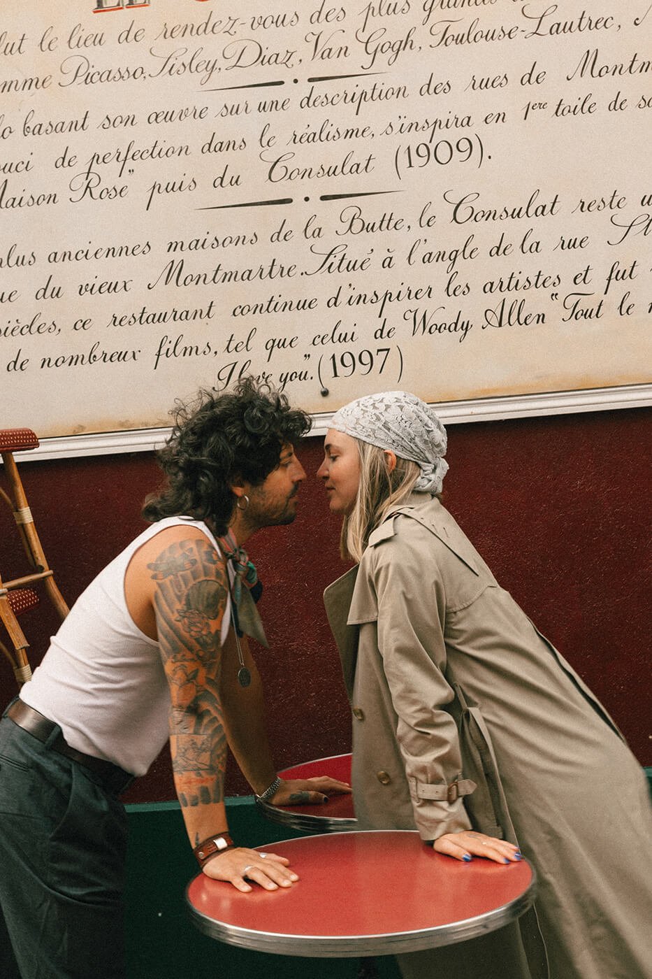 Romantic couple portrait outside a Paris café with red walls and classic bistro tables, engagement session inspiration in Montmartre.