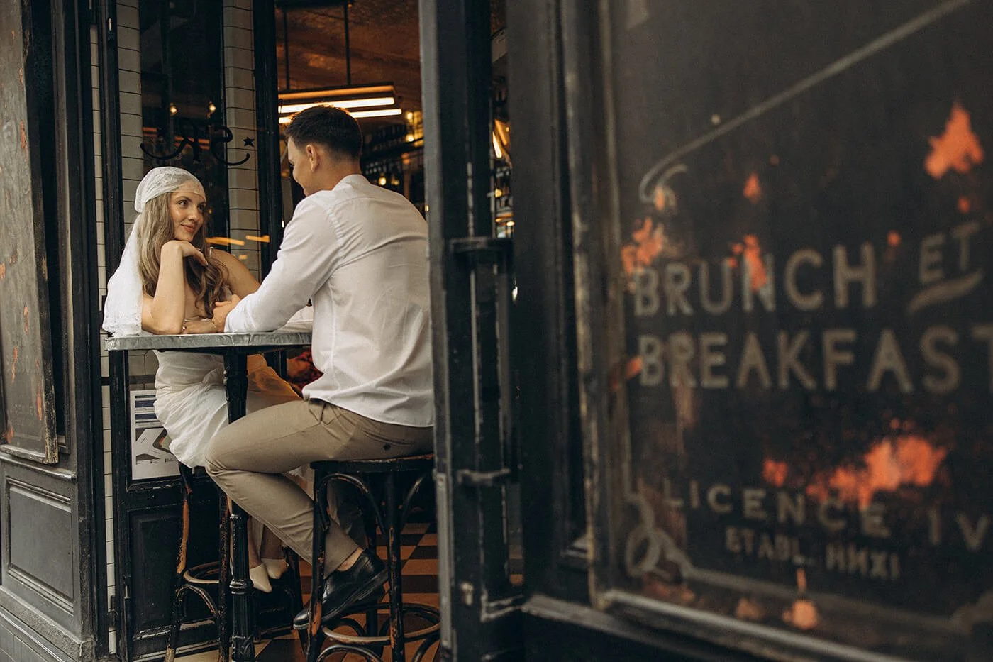 Playful couple sitting in restaurant in Ile Saint Louis during their Paris engagement session, relaxed and authentic love story photography.