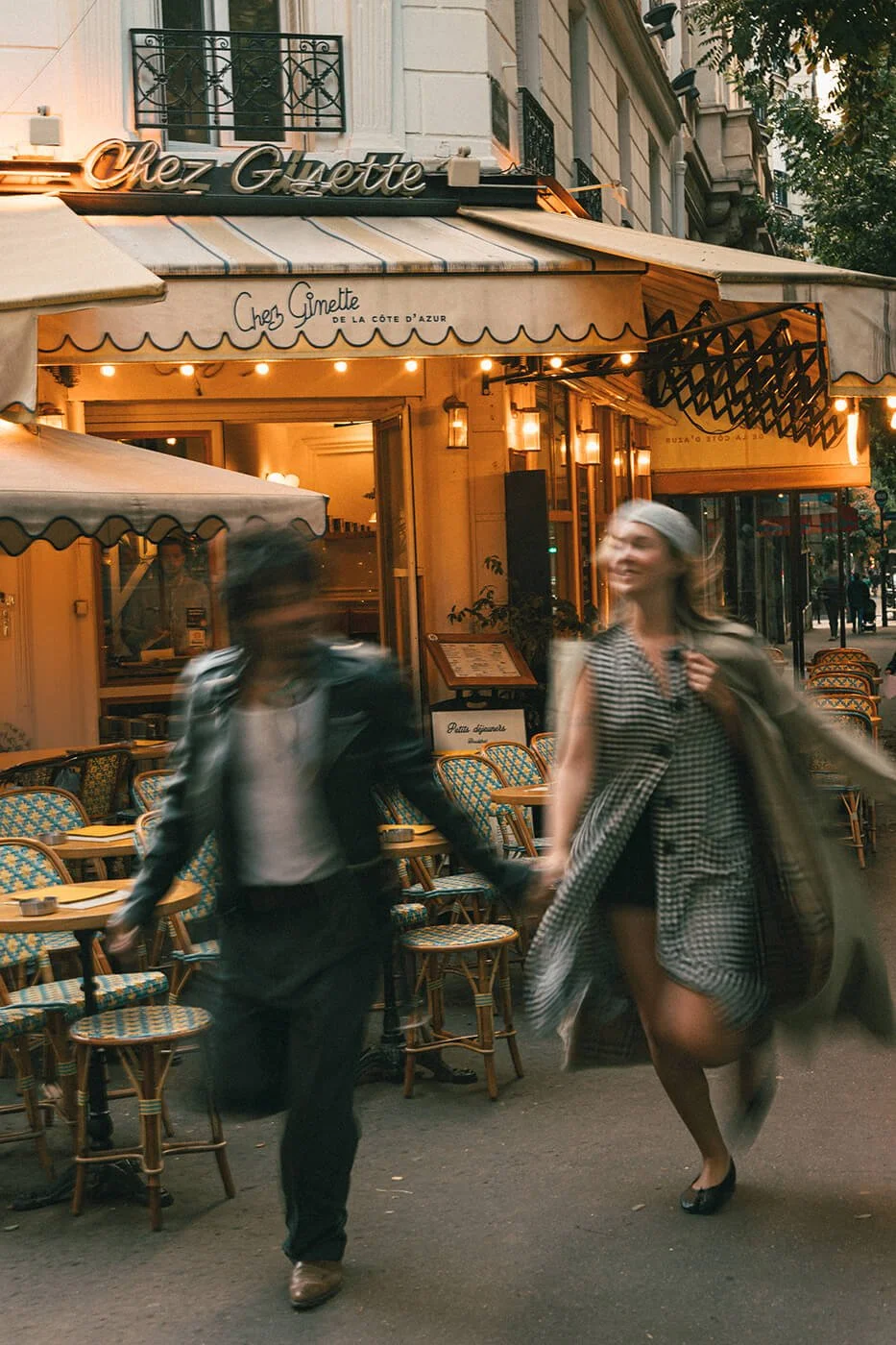 Couple crossing a Paris street near a traditional French café, documentary-style engagement session in Montmartre.