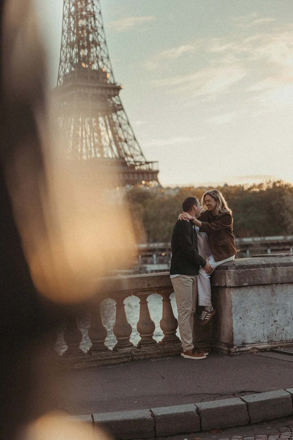 Couple photographed at sunrise in Paris with the Eiffel Tower in soft morning light.