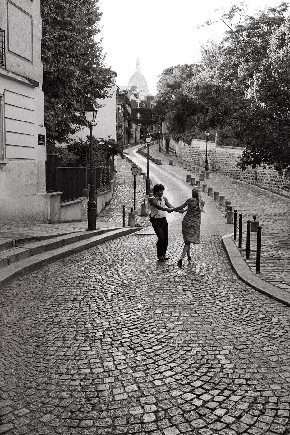 Couple twirling on cobblestone streets in Paris during a romantic engagement session, natural movement captured by a Paris engagement photographer.