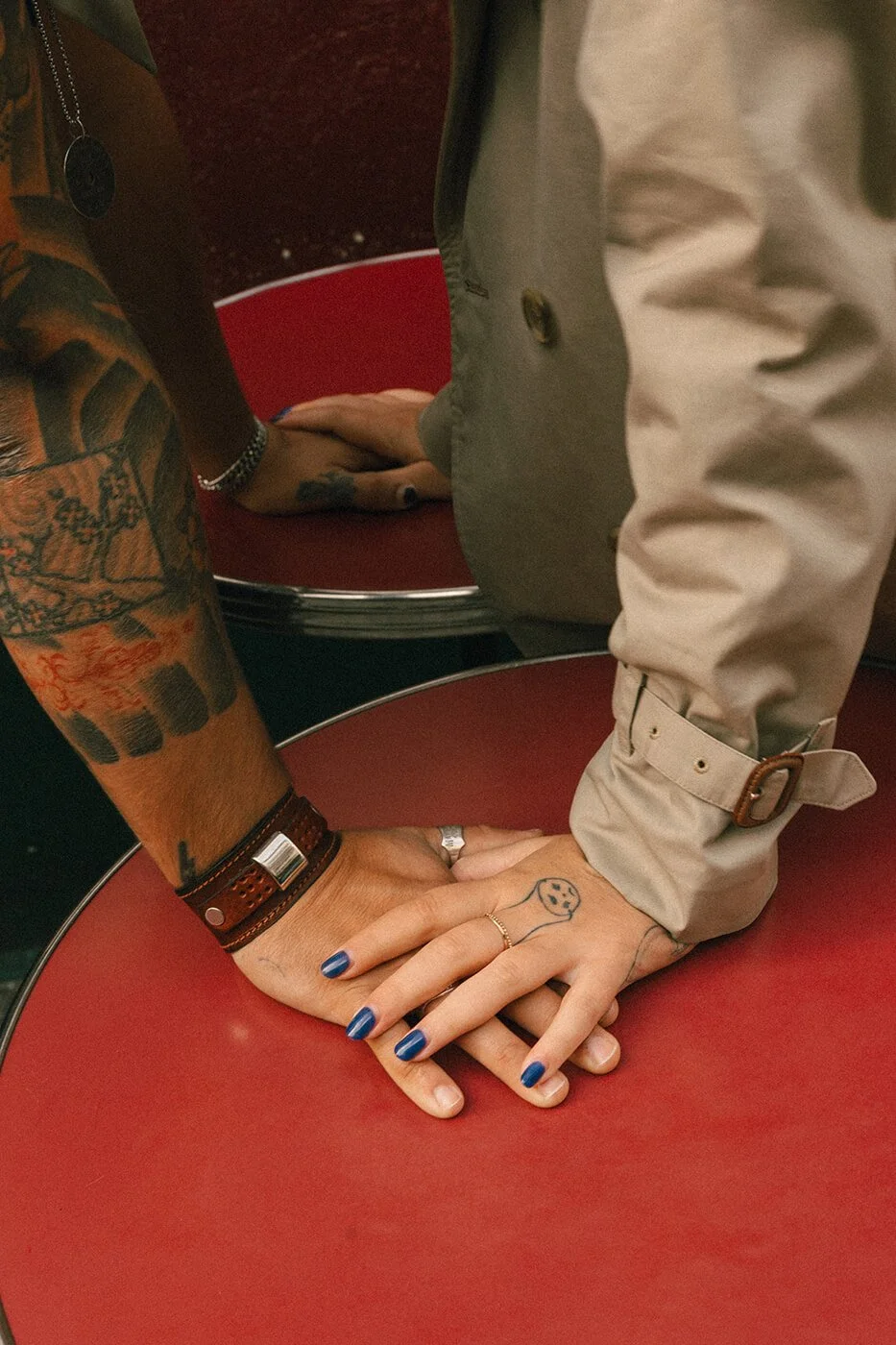 Close-up detail of couple’s hands on a red café table during their engagement session in Paris, storytelling engagement photography.