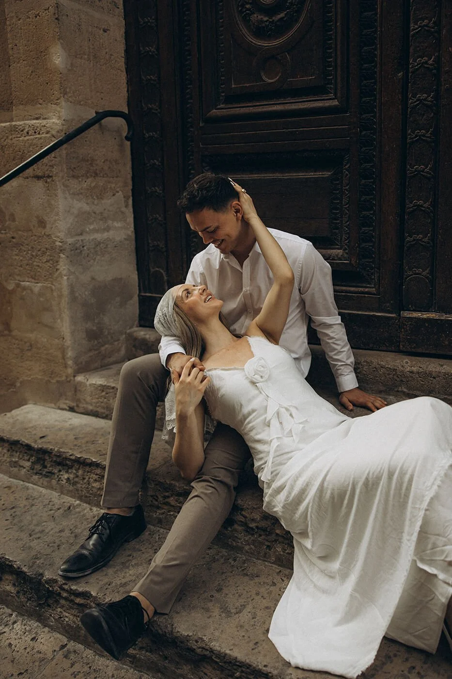Playful couple sitting on the stairs in Ile Saint Louis during their Paris engagement session, relaxed and authentic love story photography.