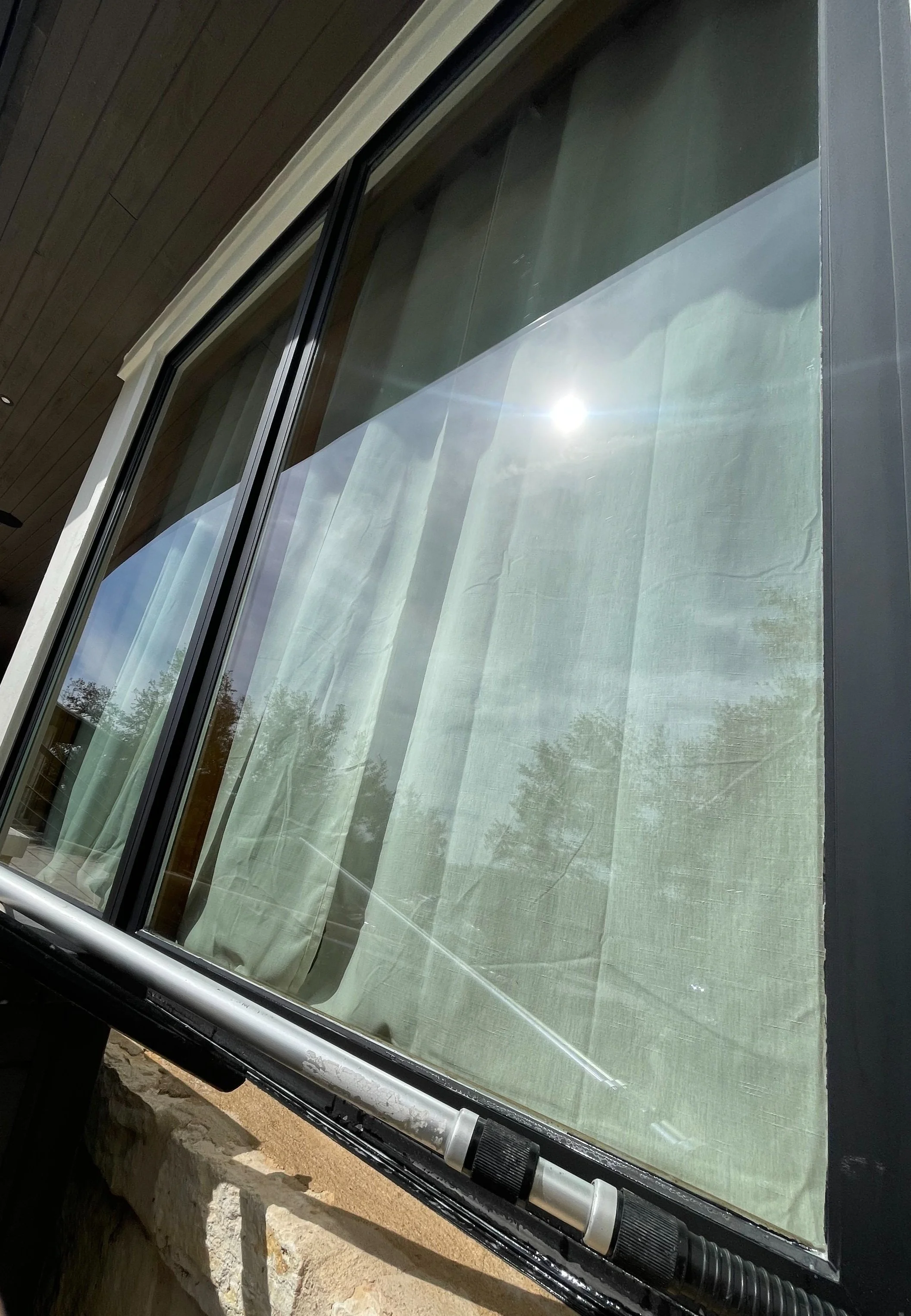 Close-up of a window with sunlight reflecting off the glass, showing trees and the sky outside.