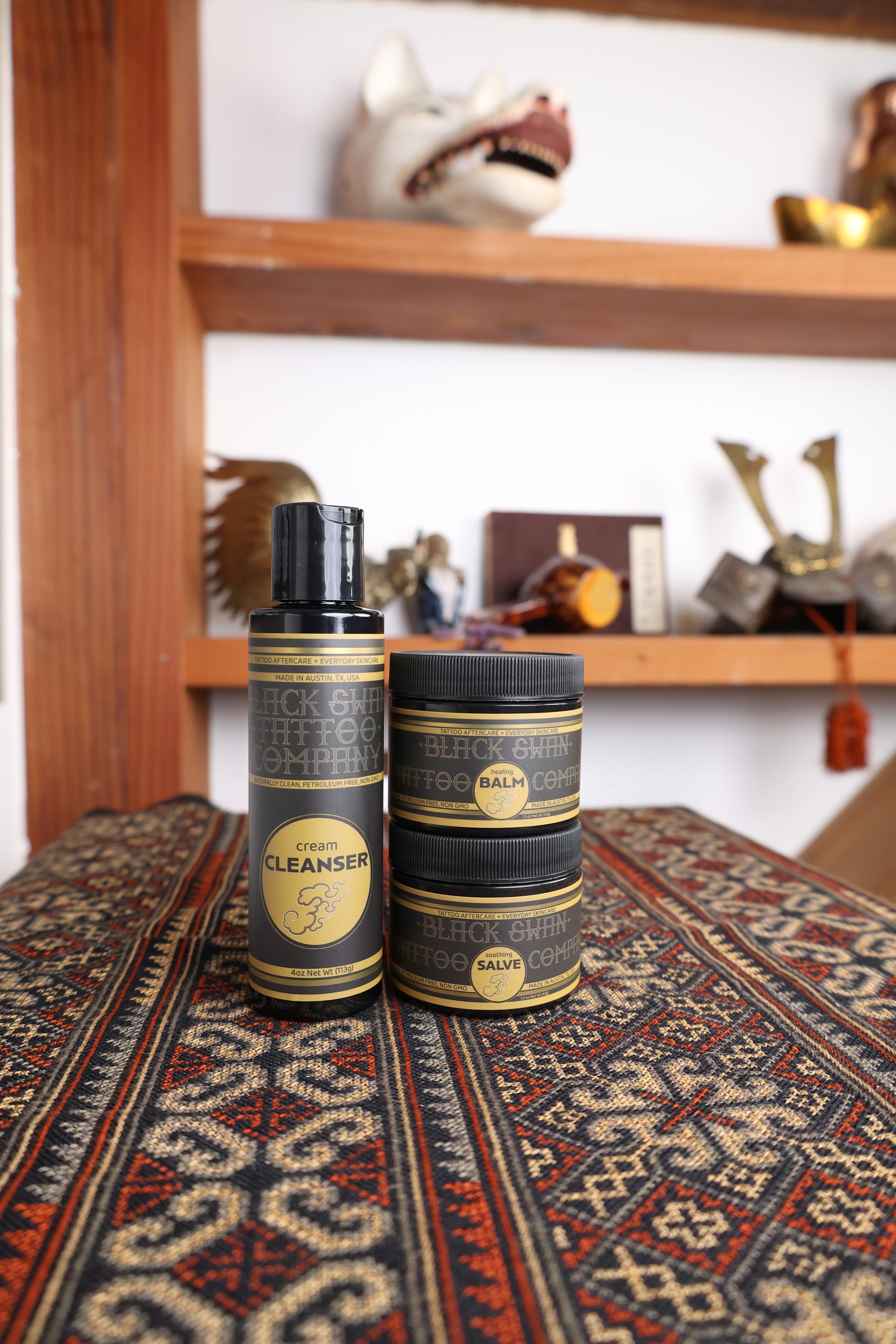 Black Swan tattoo aftercare trio on patterned textile studio setting