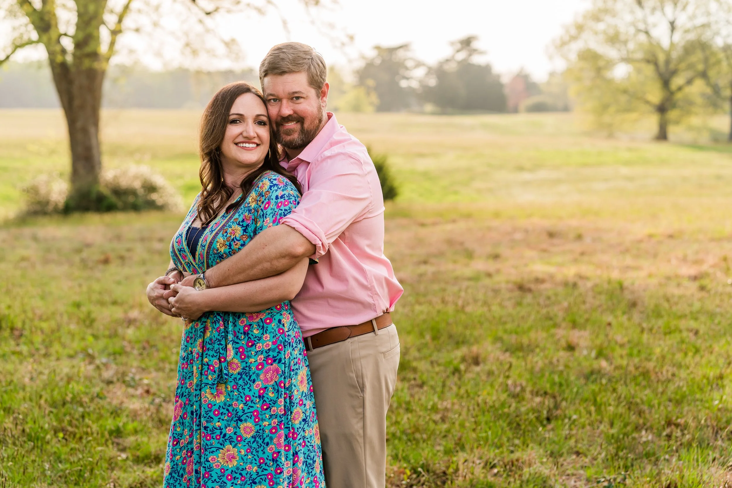 A happy couple embracing outdoors in a park on a sunny day, with trees and grass in the background.