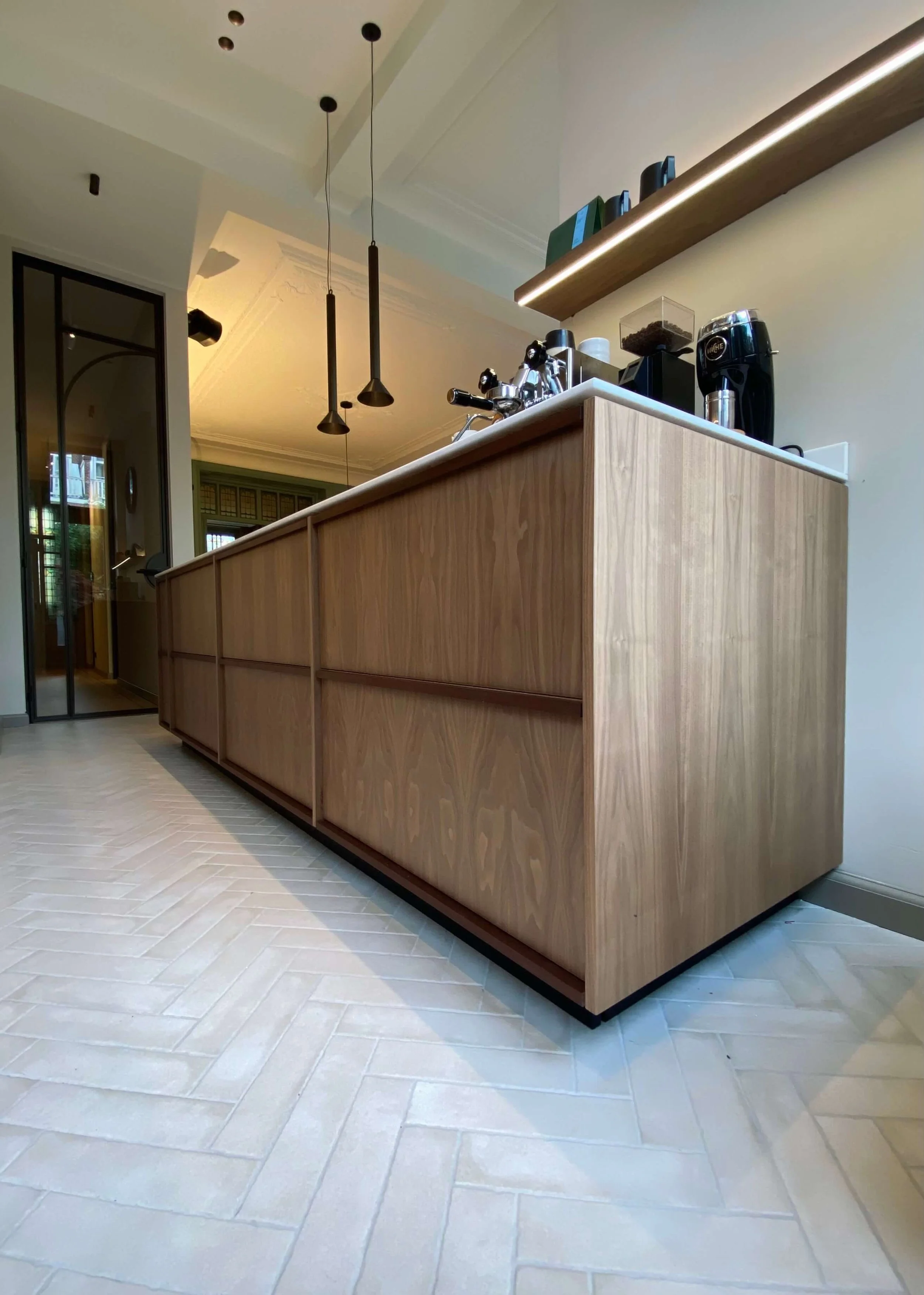 A modern kitchen island with a wood finish and white countertop, with hanging black pendant lights above, in a contemporary kitchen.
