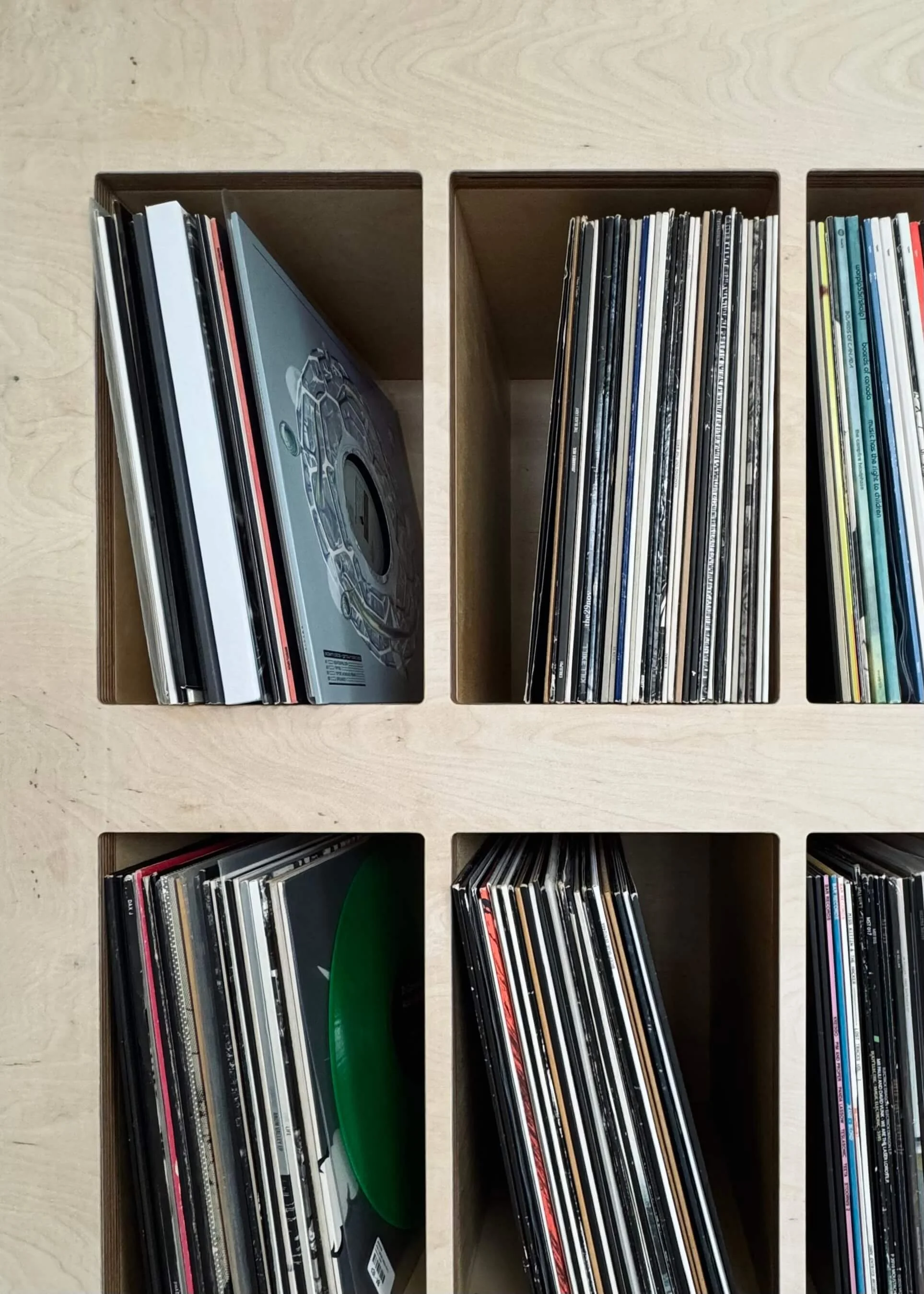 Organized vinyl record collection in wooden compartments on a light-colored wooden surface.
