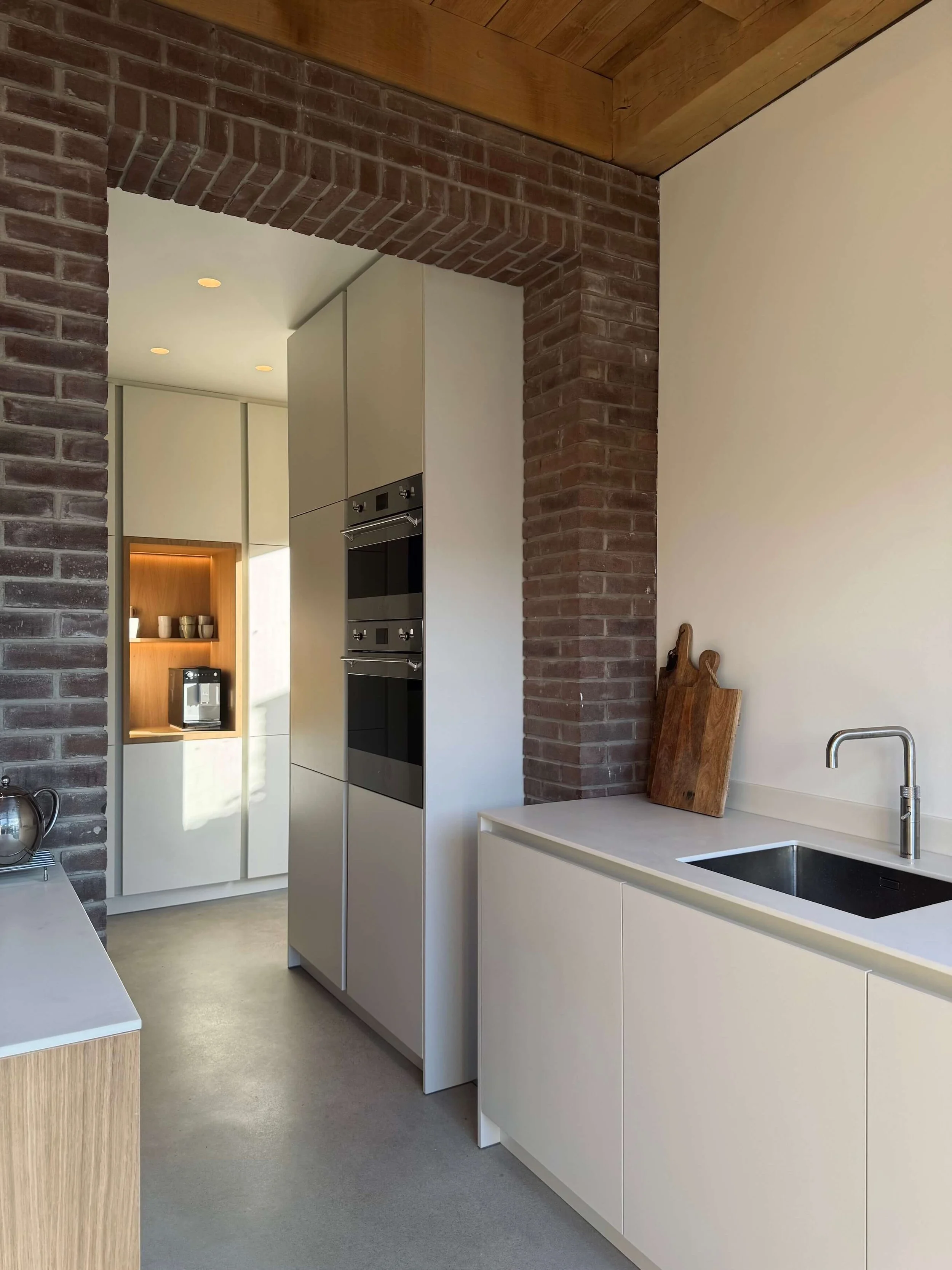 Modern kitchen with white cabinets, a black sink, a wooden cutting board, and exposed brick walls.
