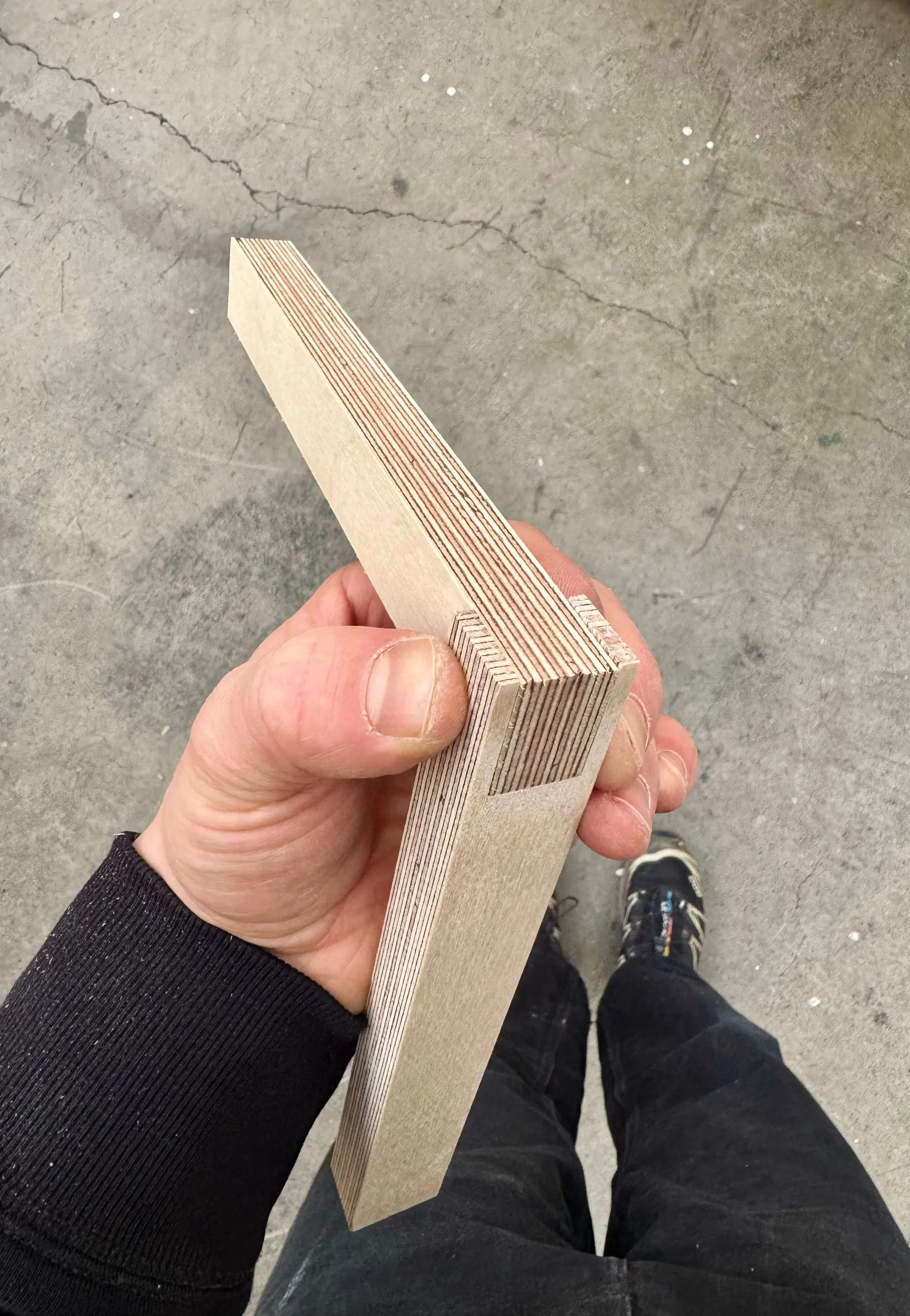 A person holding several sheets of plywood in a workshop or construction area, with a concrete floor visible.