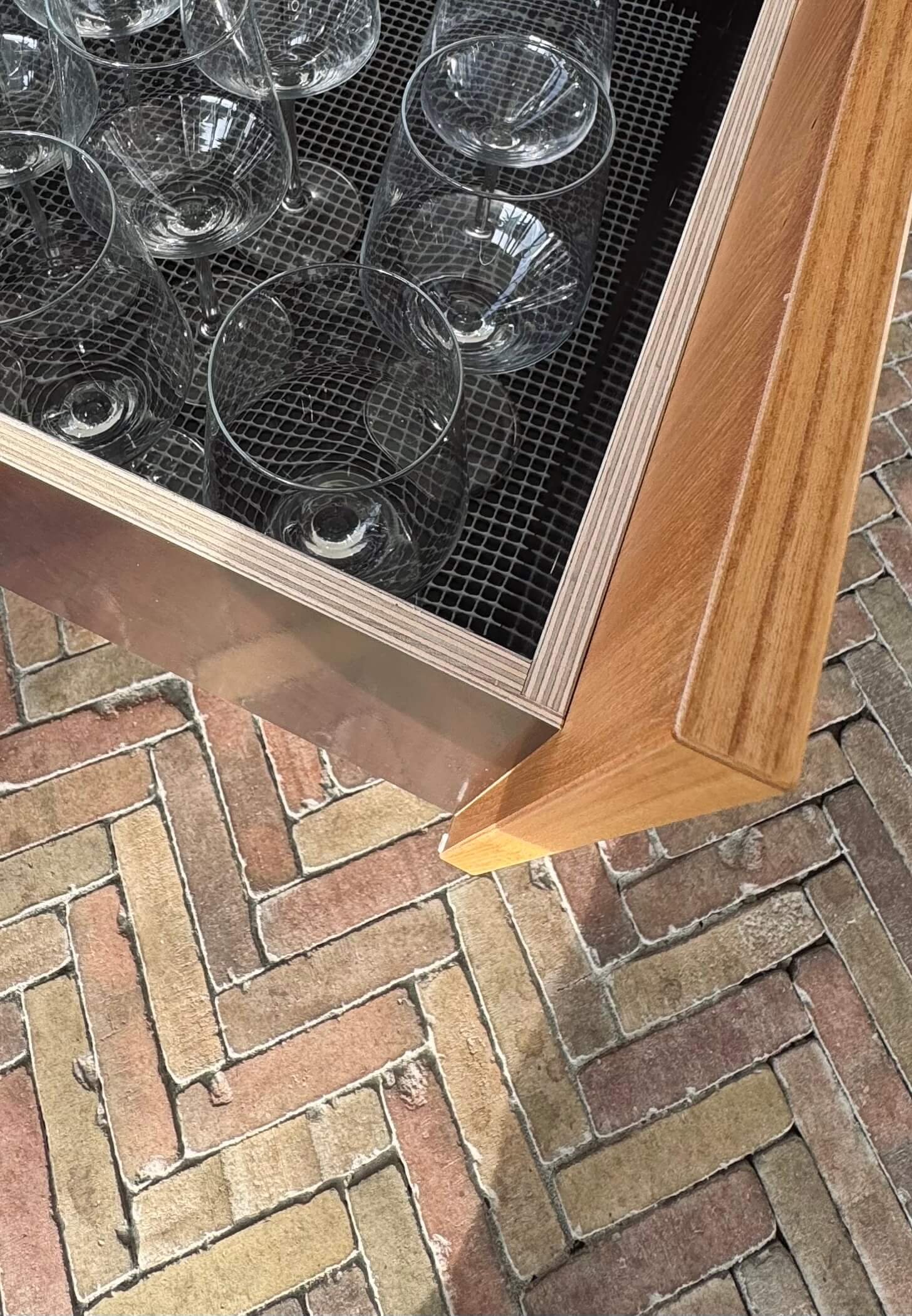 Glassware inside a wooden and metal cabinet on a brick floor.