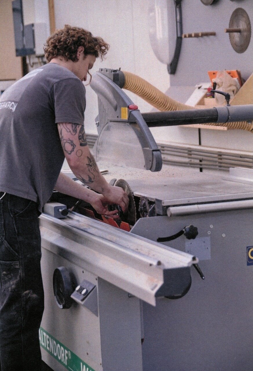 Person working with a circular saw in a workshop, surrounded by tools and equipment.