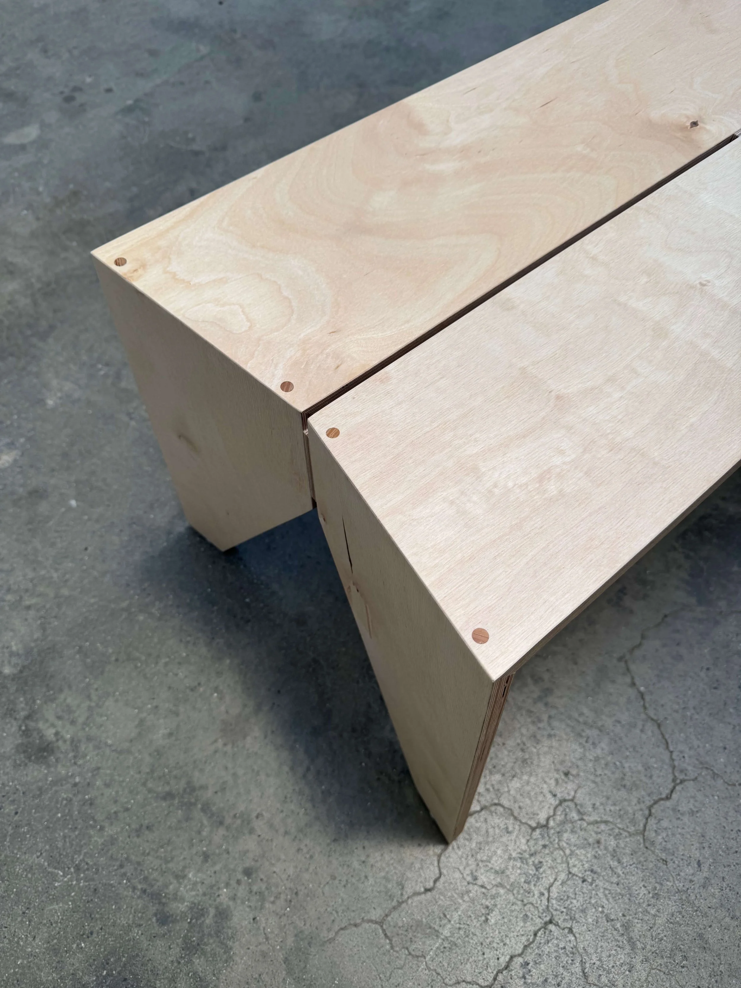 Close-up of a wooden bench with a smooth, unfinished surface, placed on a concrete floor with visible cracks.