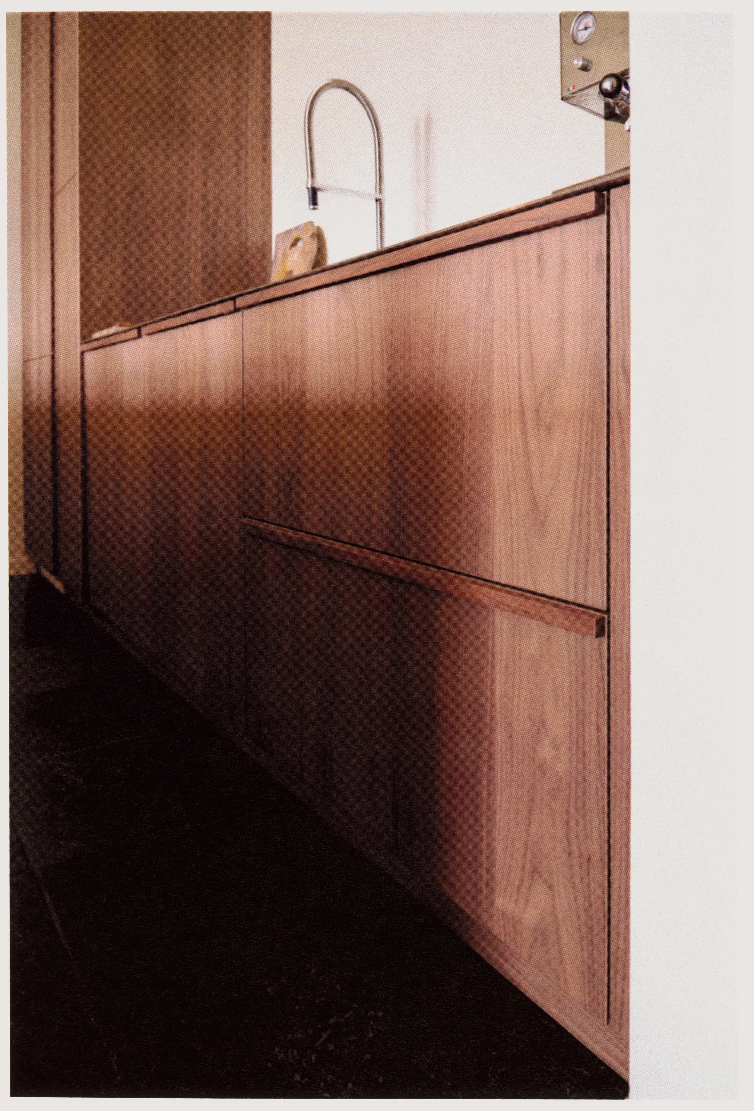 Close-up of a wooden kitchen cabinet with a countertop and a sink faucet visible in the background.