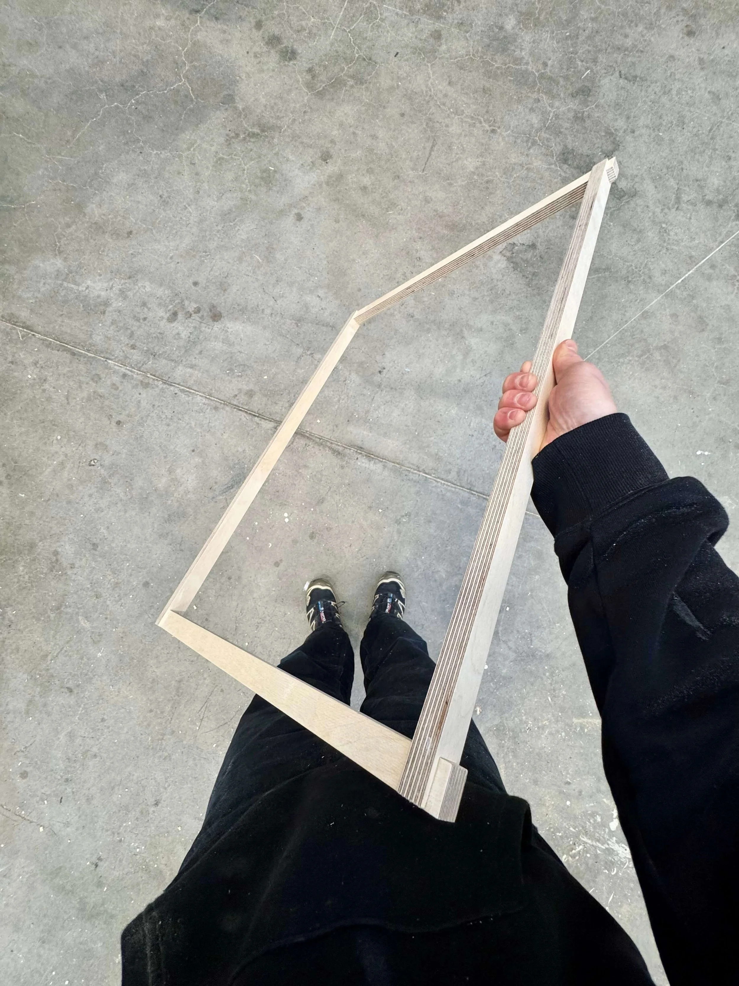Person holding a wooden frame or stencil, standing on a concrete floor.