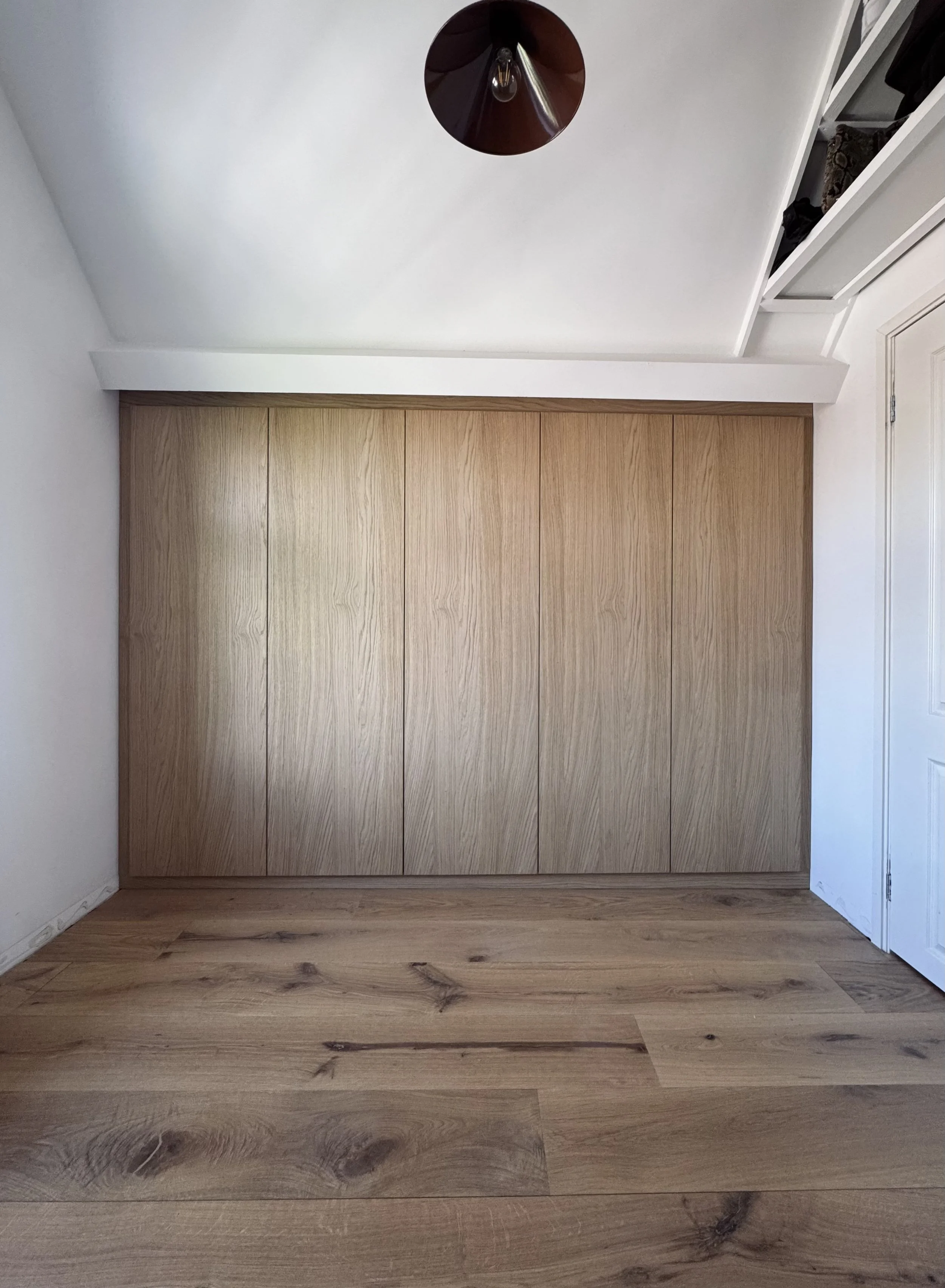 Empty room with wood closet doors, hardwood floor, white walls, and a ceiling light fixture.