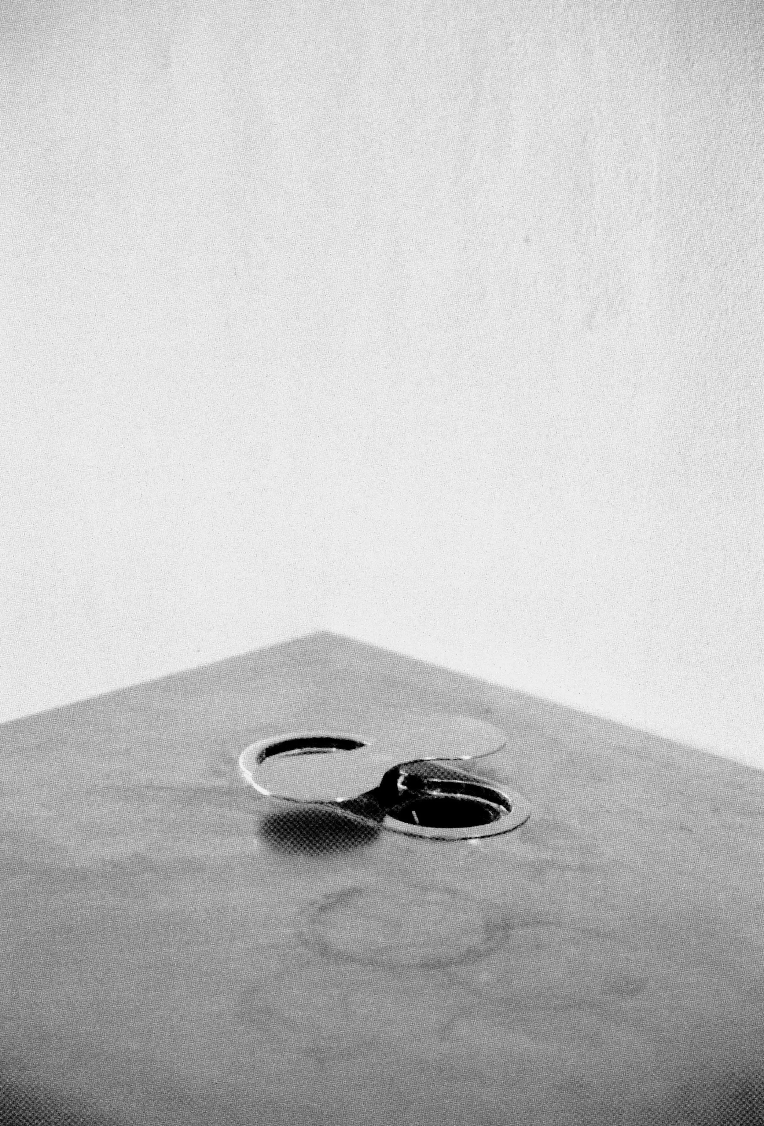 A pair of scissors resting on a wooden surface with a shadow cast beneath them, against a plain wall.