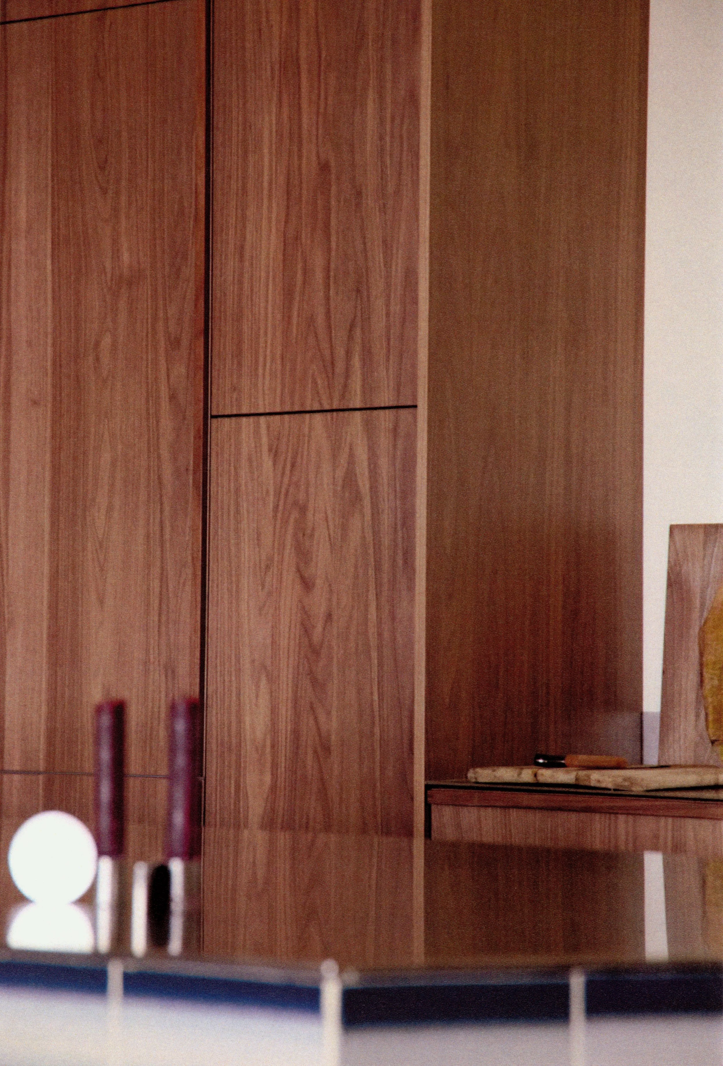 Close-up of a wooden cabinet with a small visible section of a table and items, including a white orb, two tall bottles, a remote control, and a wooden board with a picture frame.