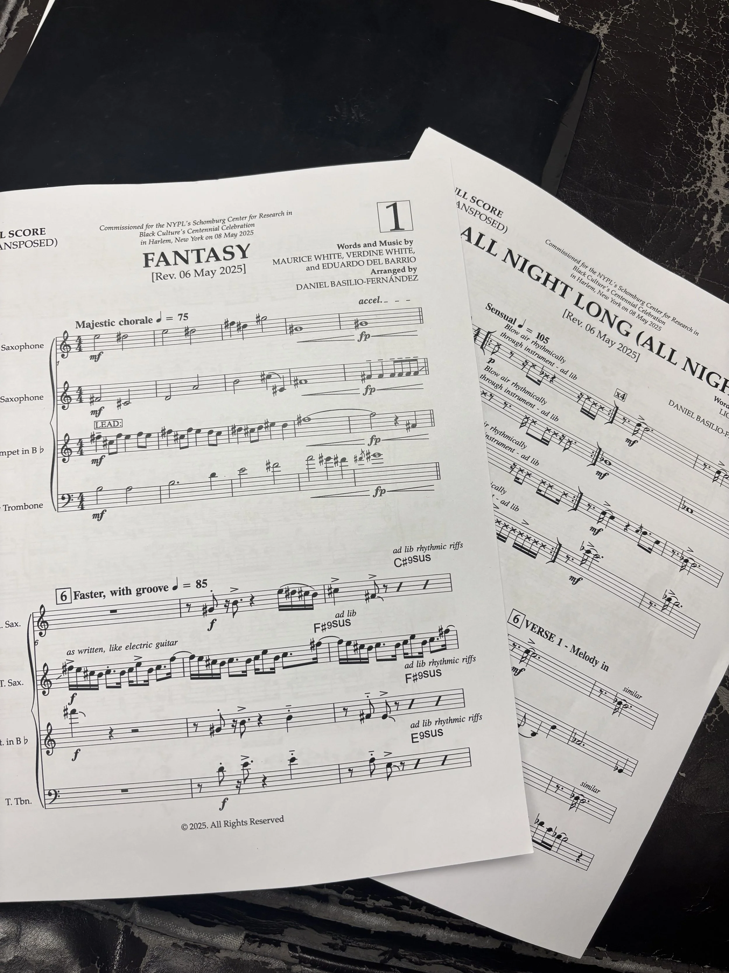 Two sheets of musical scores for jazz compositions titled "Fantasy" and "All Night Long" on dark surface.