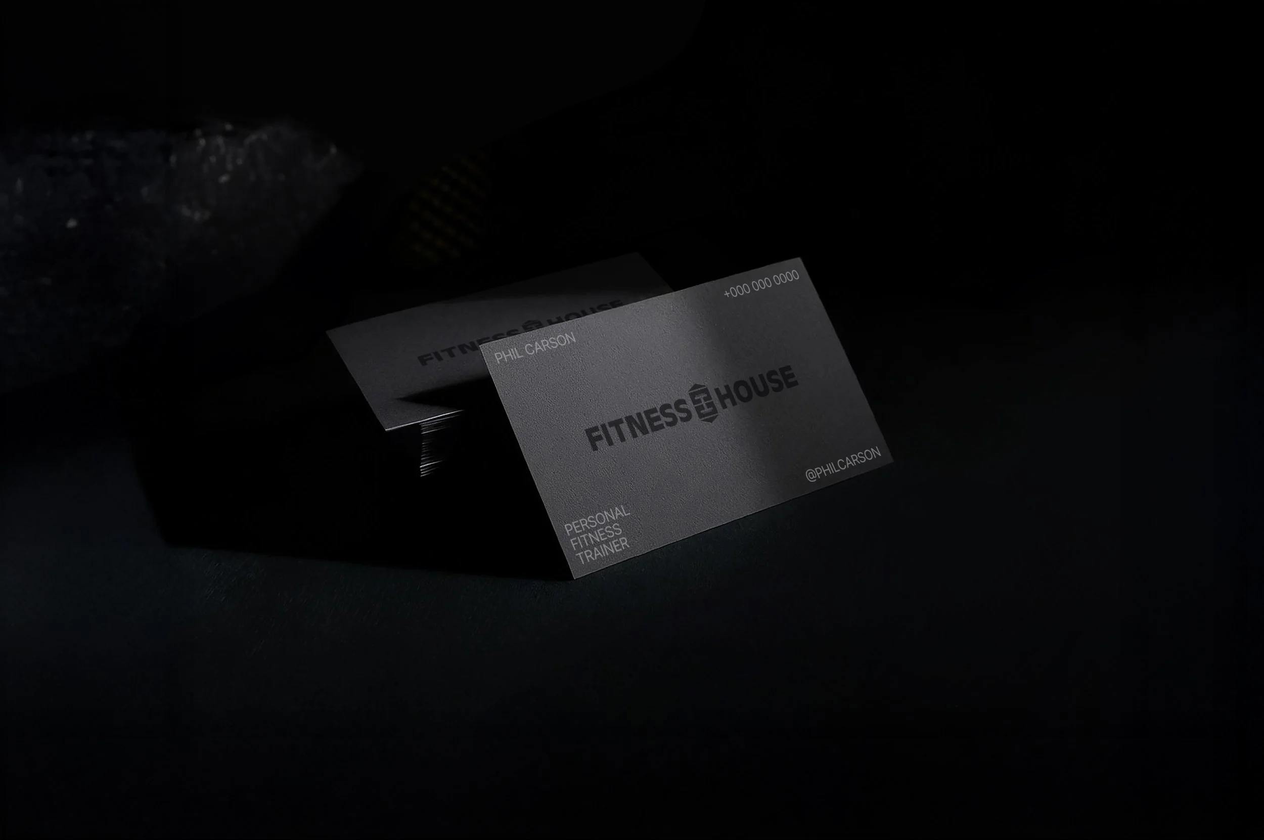 A business card for Fitness House, a personal fitness trainer placed on a dark surface in a dimly lit environment.