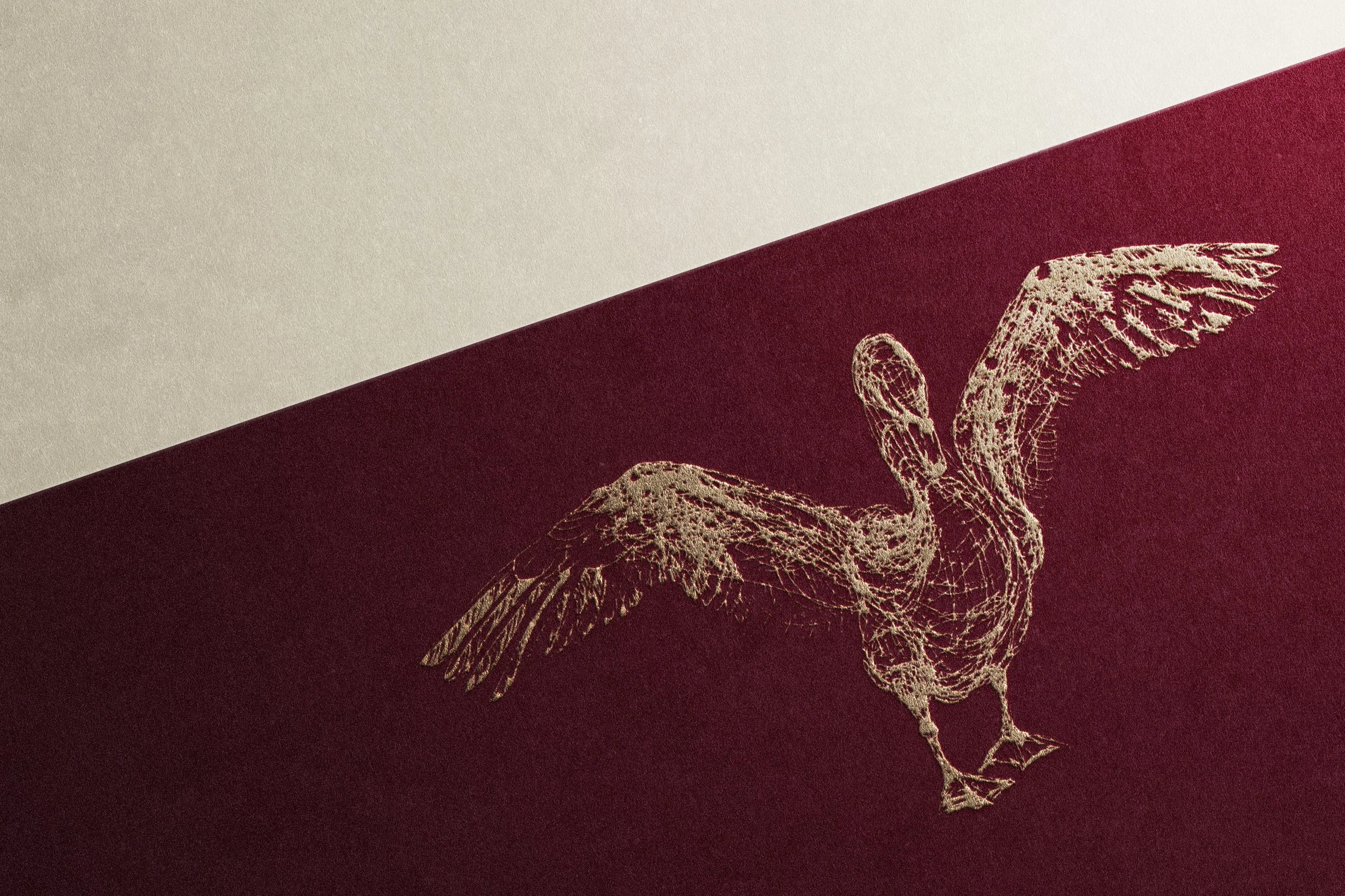 Close-up of a gold foil design of a bird with outstretched wings on a burgundy book cover.