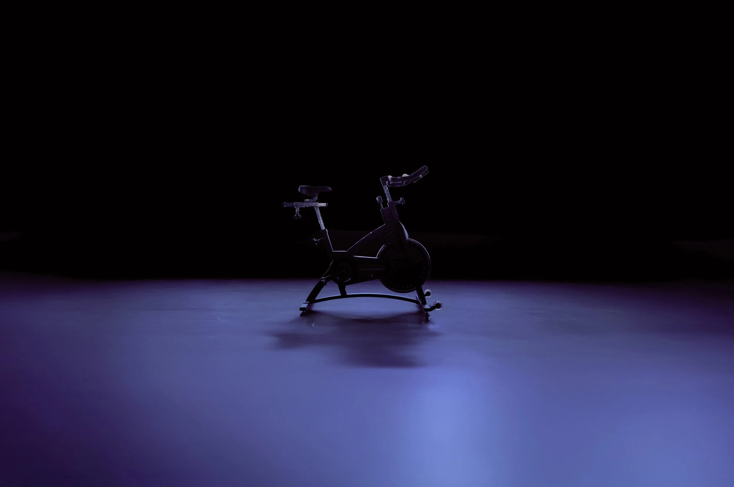 A stationary exercise bike in a dark room with purple lighting, creating a minimalist and modern atmosphere.