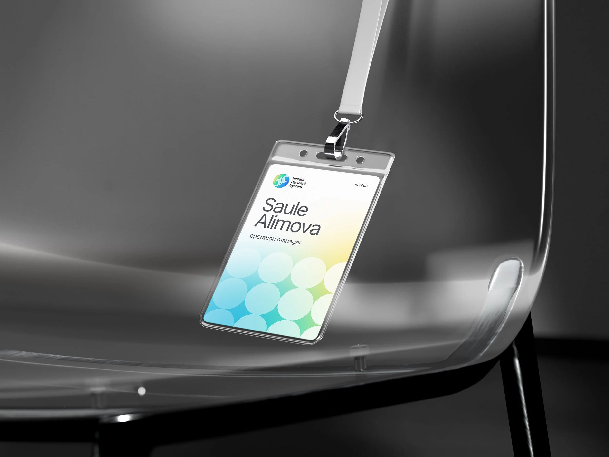 A close-up of a black machine with a name badge hanging from a white lanyard that reads 'Saule Alimova, operation manager' and features a colorful logo for the 'Instant Payment System.'
