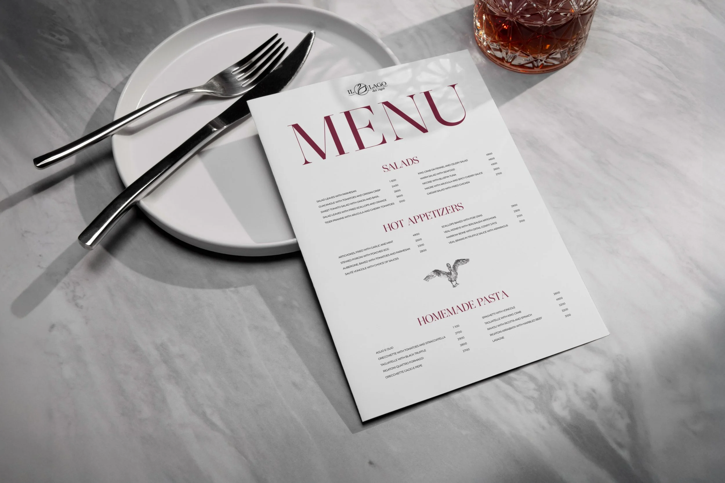 A white plate with a fork and knife, a menu paper with the title 'MENU,' and a glass of dark beverage on a marble table.