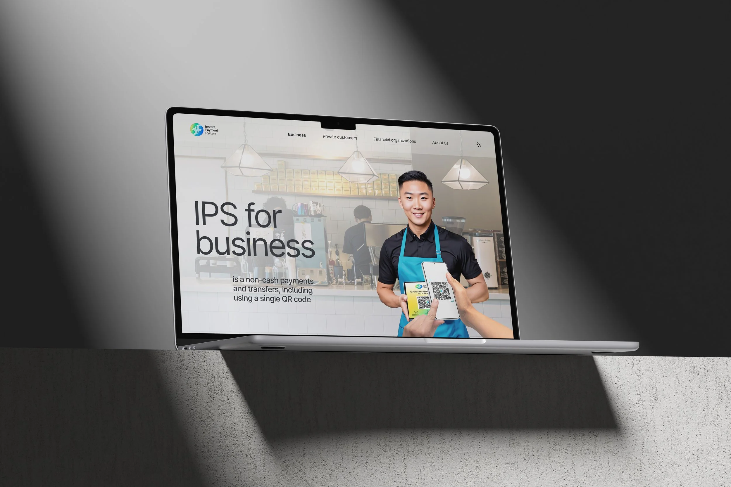A laptop displaying a website about non-cash payments for businesses, with a person holding a smartphone showing a QR code, in a modern environment.