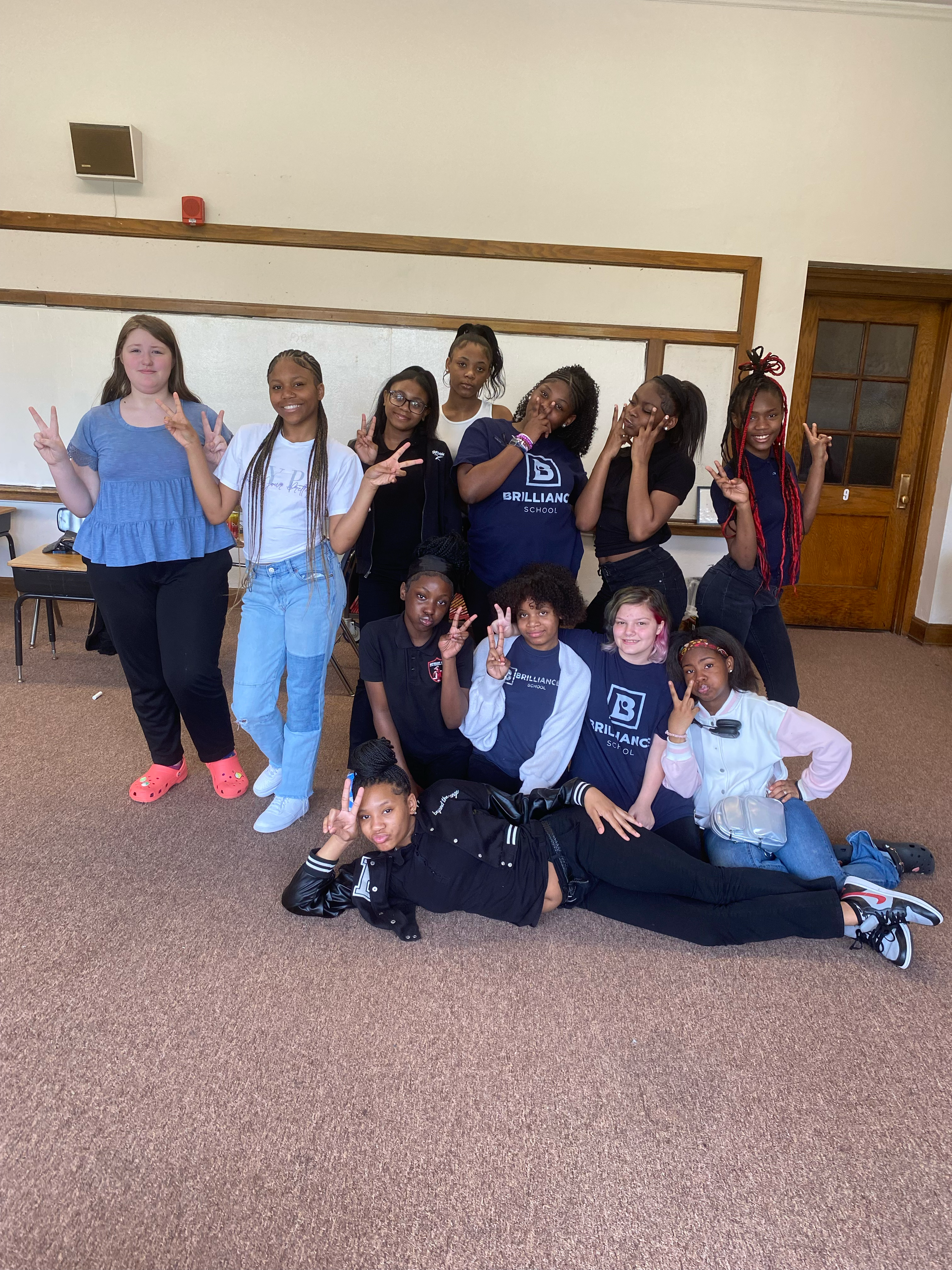 Group of ten girls in a classroom, posing and making peace signs, some sitting and some standing.