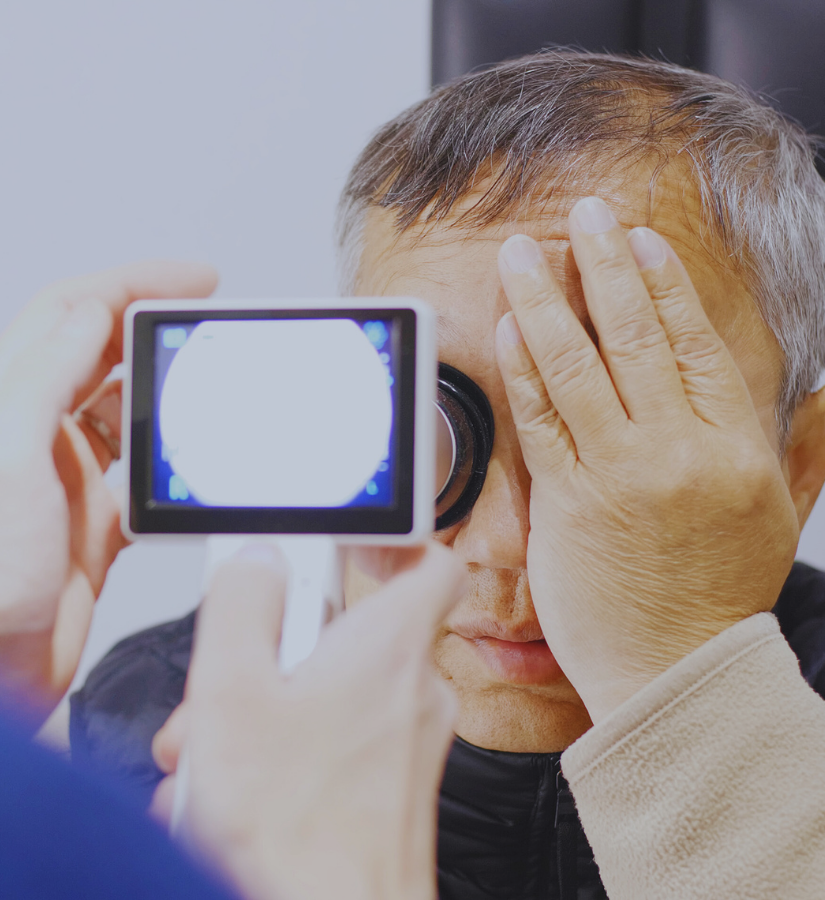 A man gets his eye examined with a handheld device by a healthcare professional