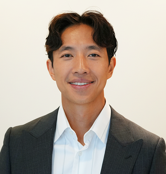 Portrait of a young man in a suit smiling at the camera against a plain background.