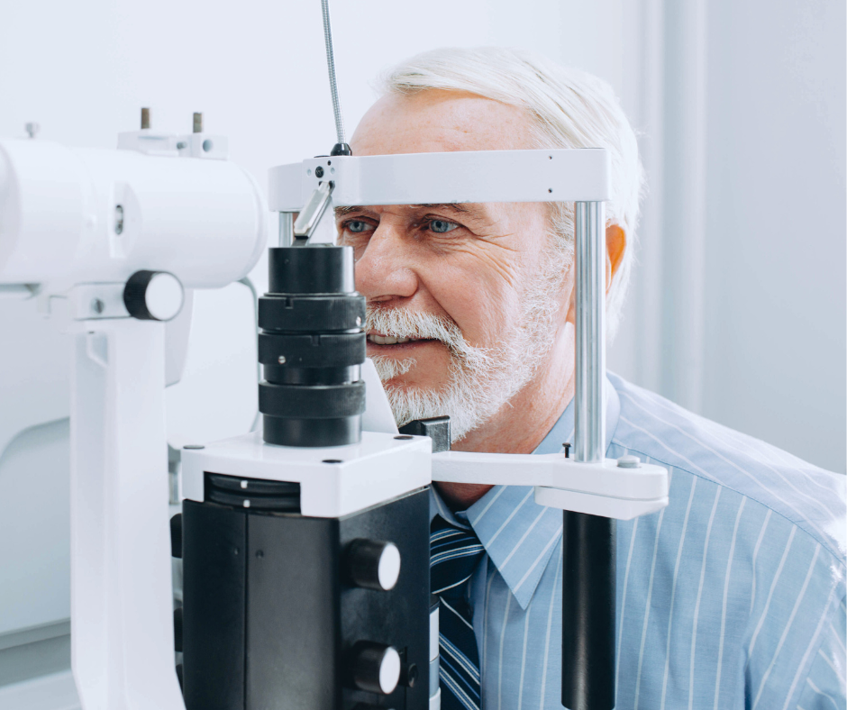 An older man with gray hair and a beard getting an eye exam using a slit lamp in an optometrist's office.