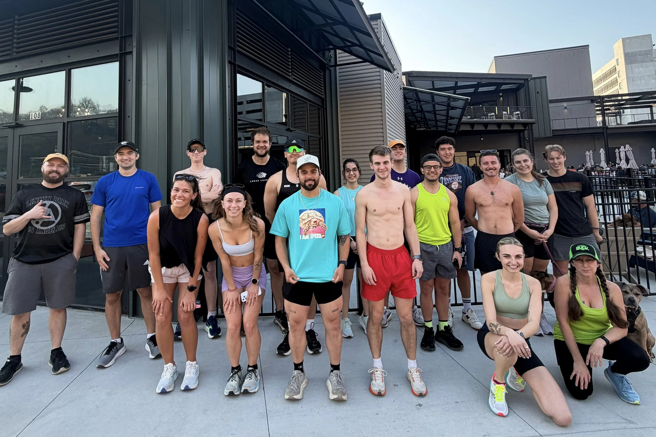 Group of people gathered outside a building at night, some in athletic clothing, celebrating after a run or marathon, with a sign that reads "Last Day of Autumn Brewing" above the entrance.