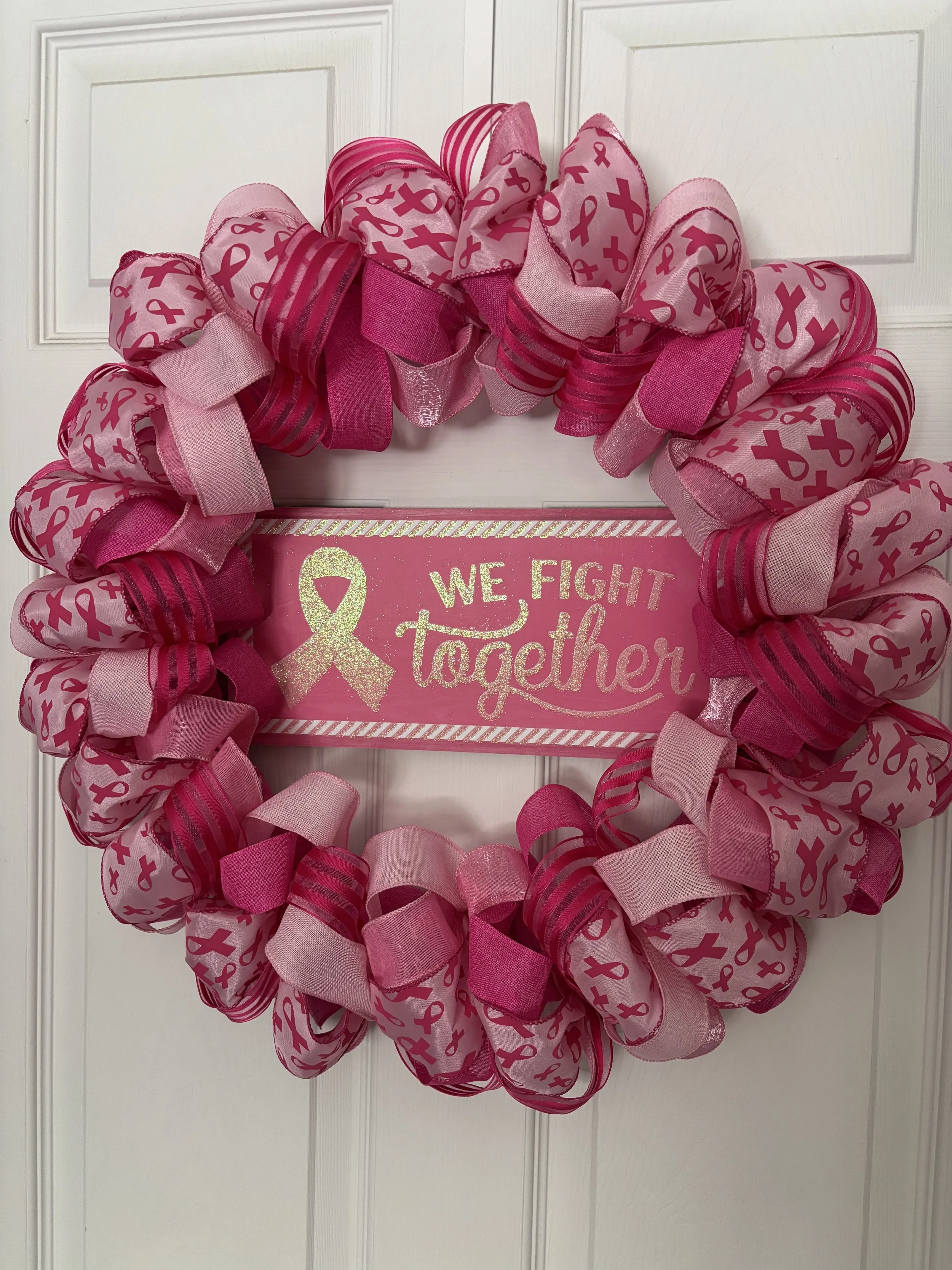 Pink and red ribbon wreath with pink bows signifying breast cancer on the pink ribbon and a pink sign in the middle with gold letters that says We Fight Together and a gold breast cancer ribbon.