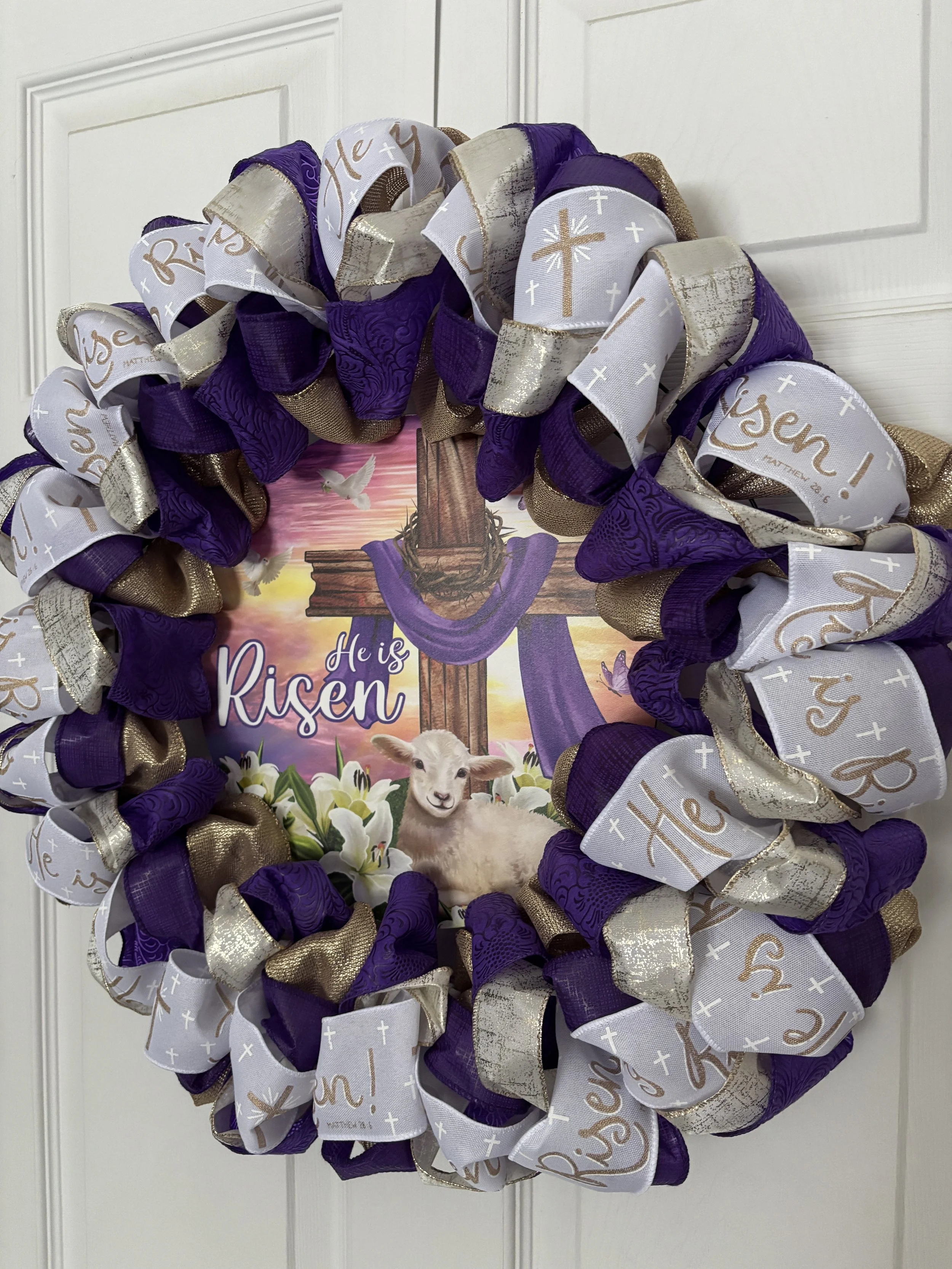 a blend of purple, gold, and white ribbons with a gold cross and “He is Risen” on the white ribbon.