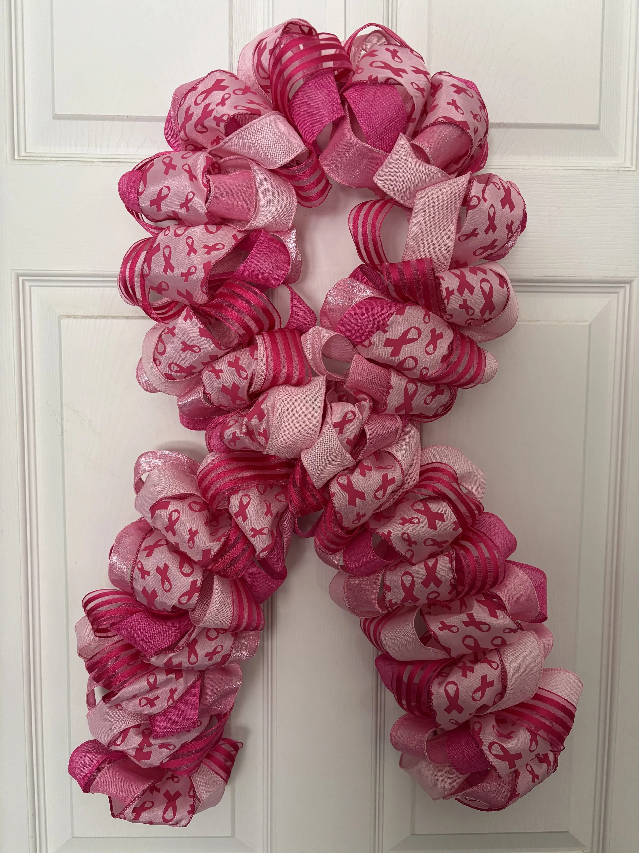 Light and dark pink ribbon with dark pink ribbon shapes on pink ribbon.  Wreath is shaped like a bow to mimic the breast cancer symbol.
