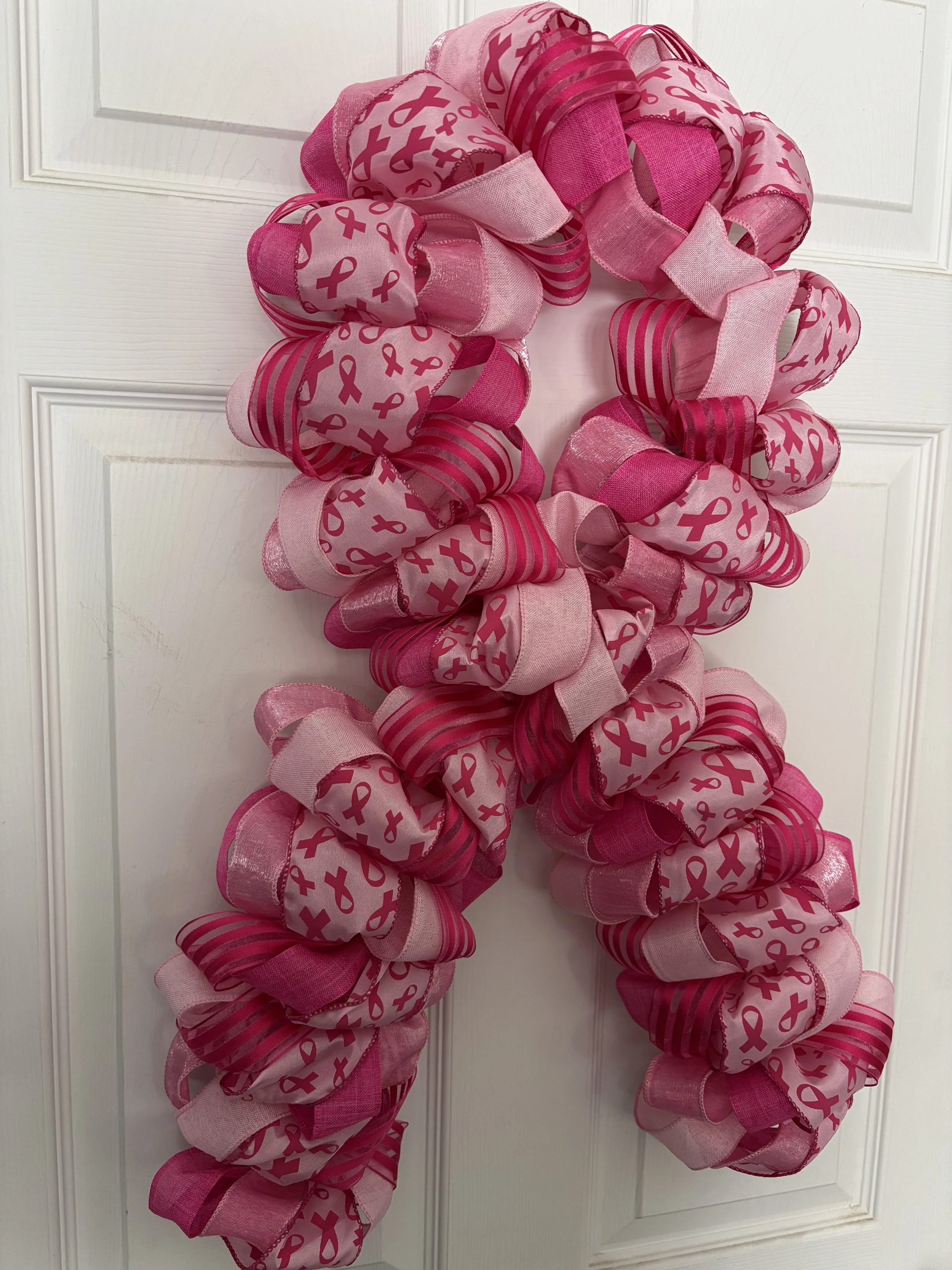 Light and dark pink ribbon with dark pink ribbon shapes on pink ribbon.  Wreath is shaped like a bow to mimic the breast cancer symbol.