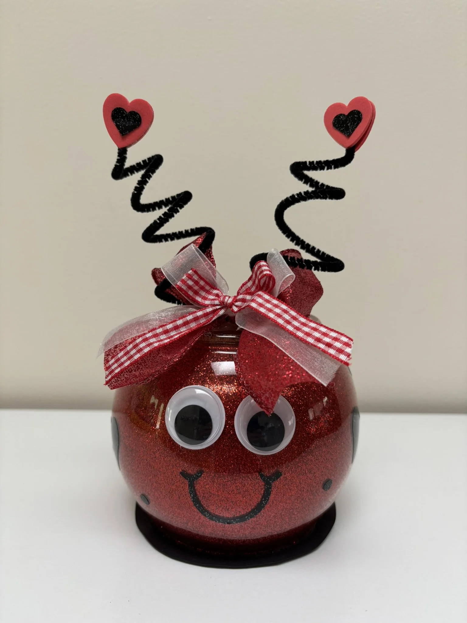Red glass figurine with big googly eyes, red and white bow, and black antennae with hearts on them
