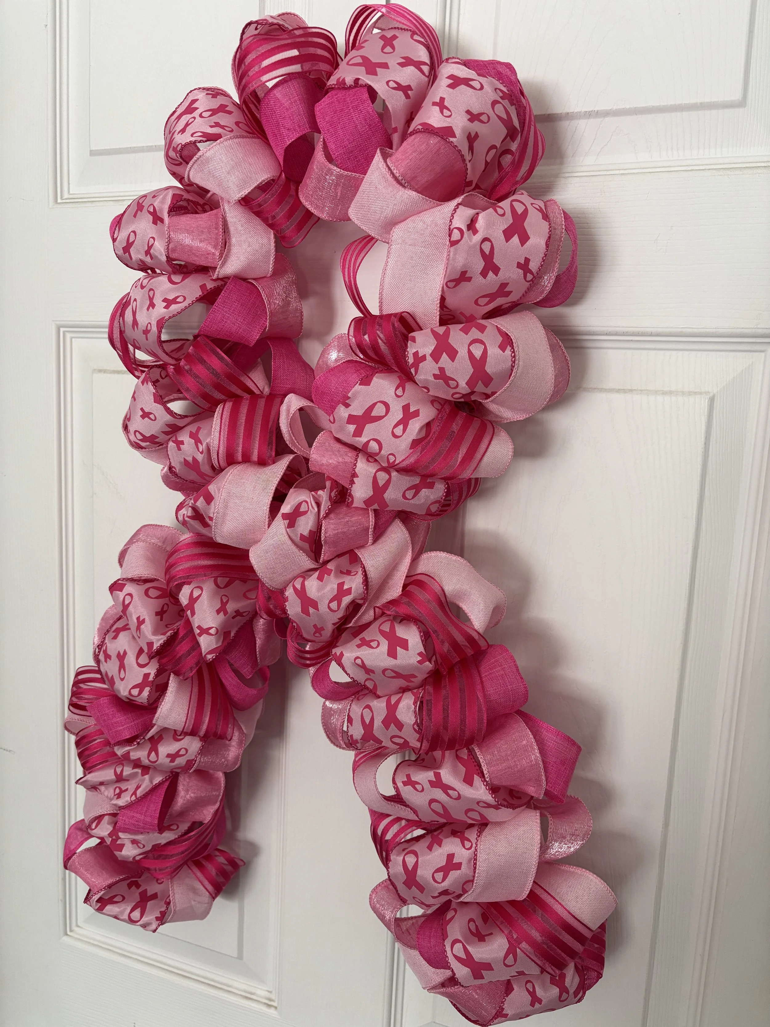 Light and dark pink ribbon with dark pink ribbon shapes on pink ribbon.  Wreath is shaped like a bow to mimic the breast cancer symbol.