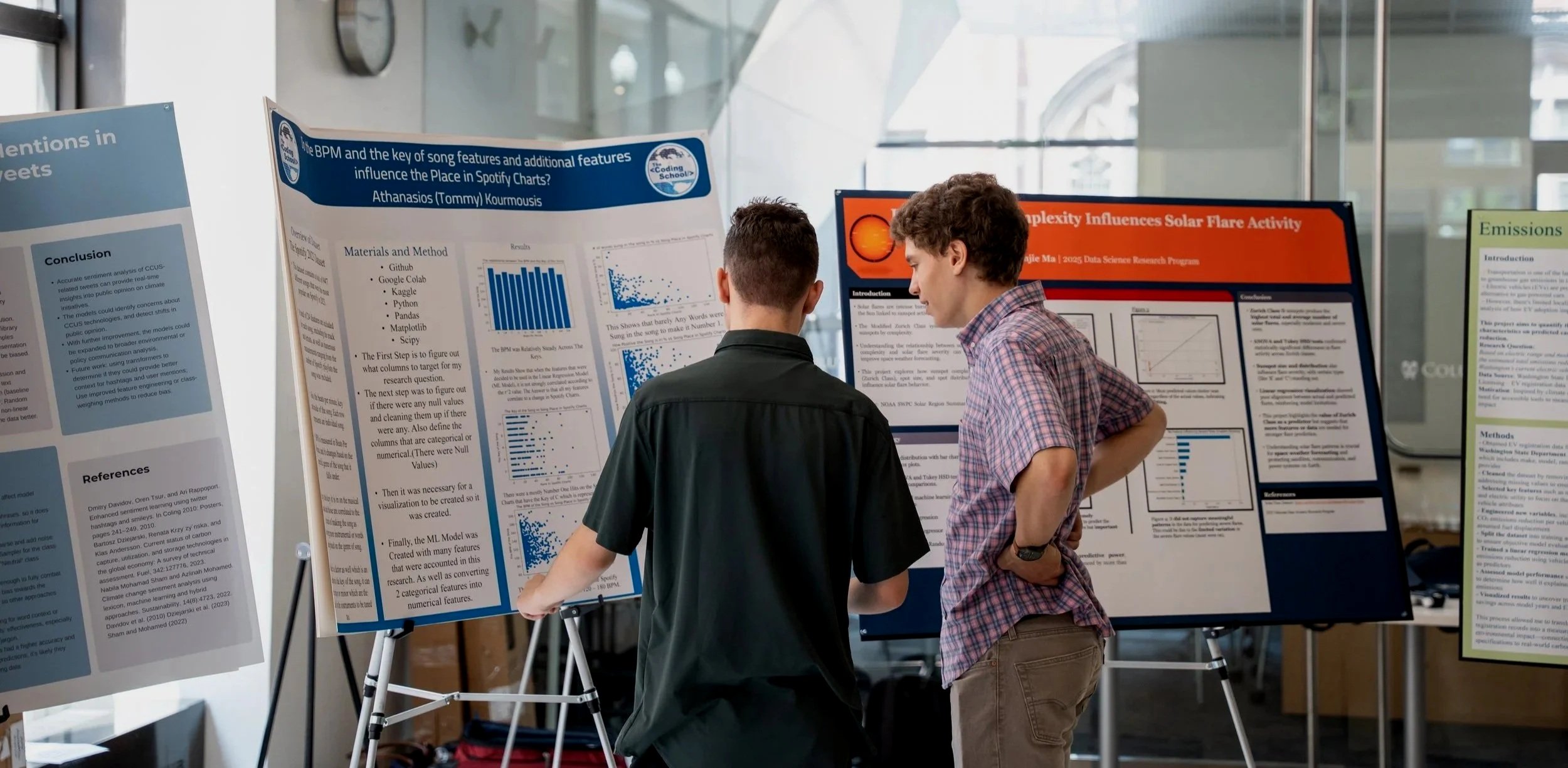Two young men standing in front of scientific research posters at an academic conference, discussing the content of the posters in a modern indoor setting.