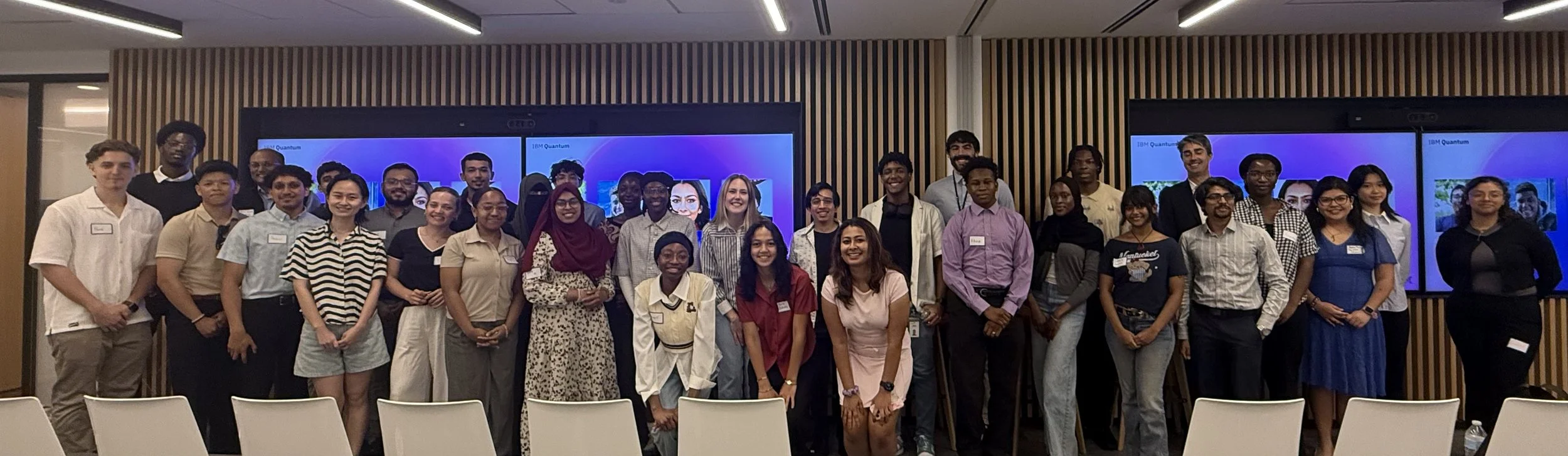 Group of diverse young adults standing in front of presentation screens in a conference room.