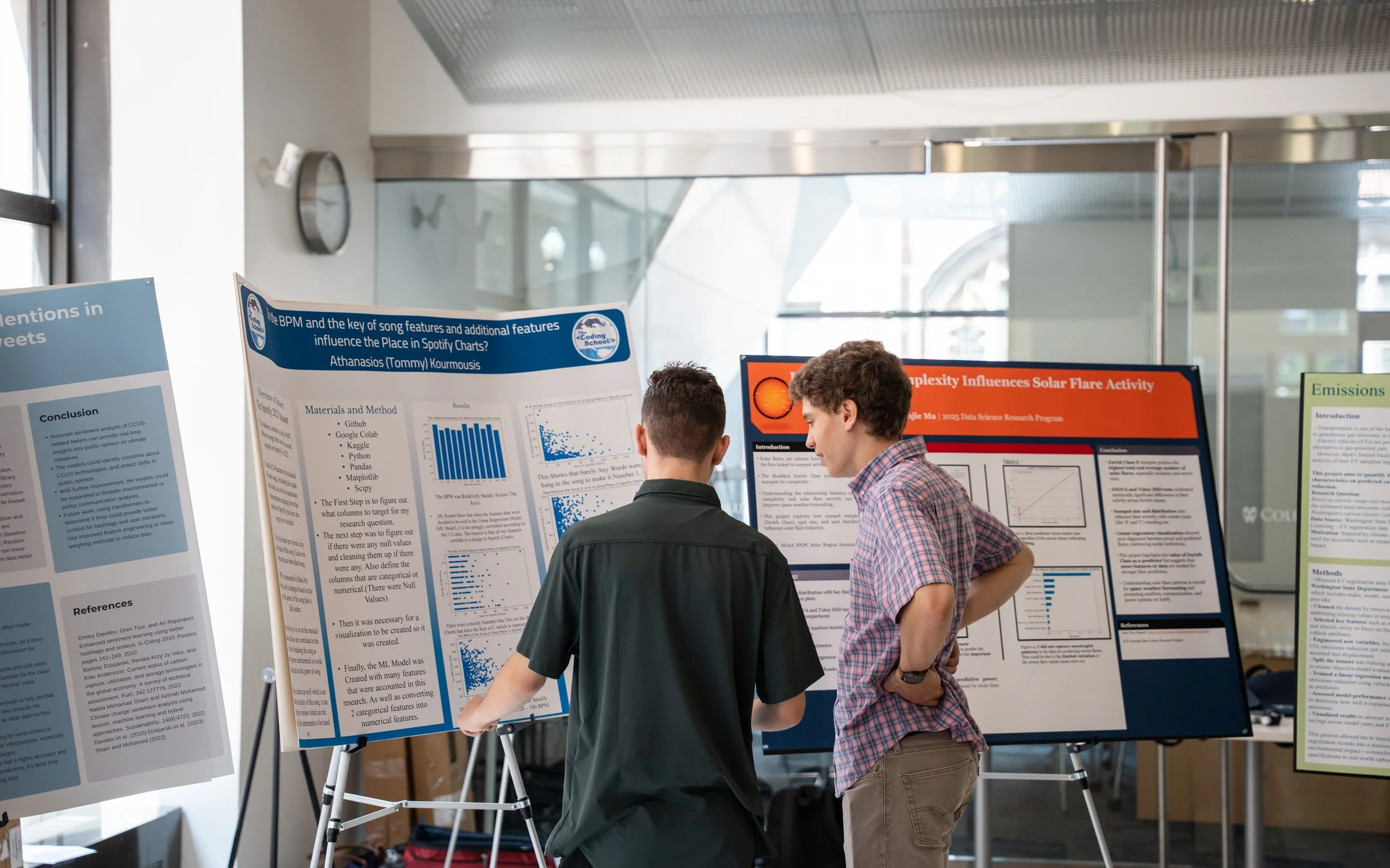 Two young men are standing in front of scientific research posters at an indoor academic conference, discussing the research.