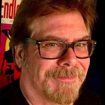 Close-up of a middle-aged man with glasses, a beard, and brown hair, smiling at the camera.