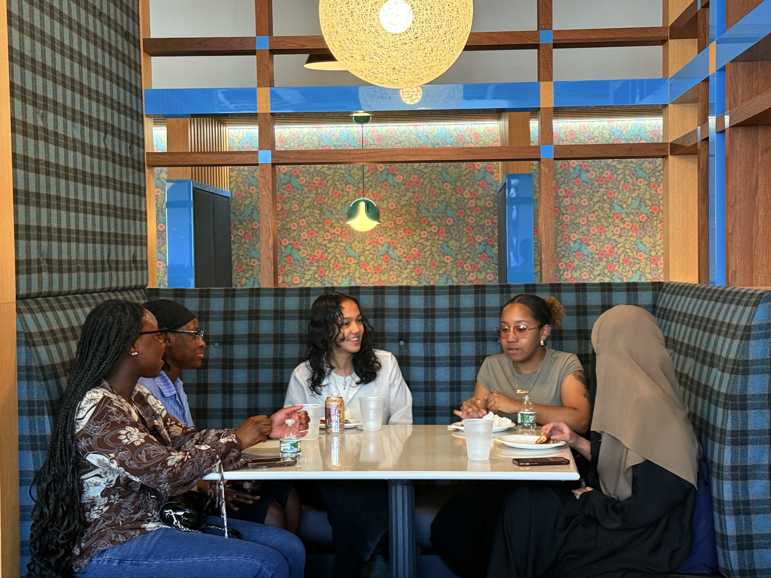 Five women sitting at a restaurant table, talking and enjoying drinks.