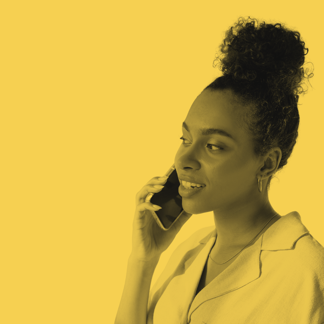 A woman with curly hair in a bun, smiling while talking on a mobile phone against a yellow background.