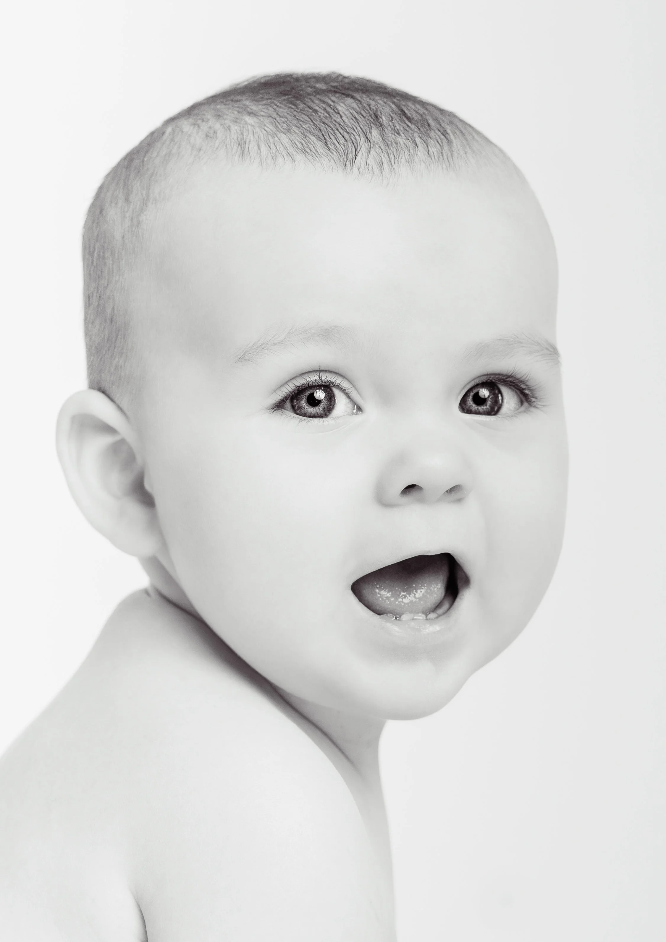 Close-up of a child's face with a surprised or excited expression, mouth open, and eyes wide in black and white.
