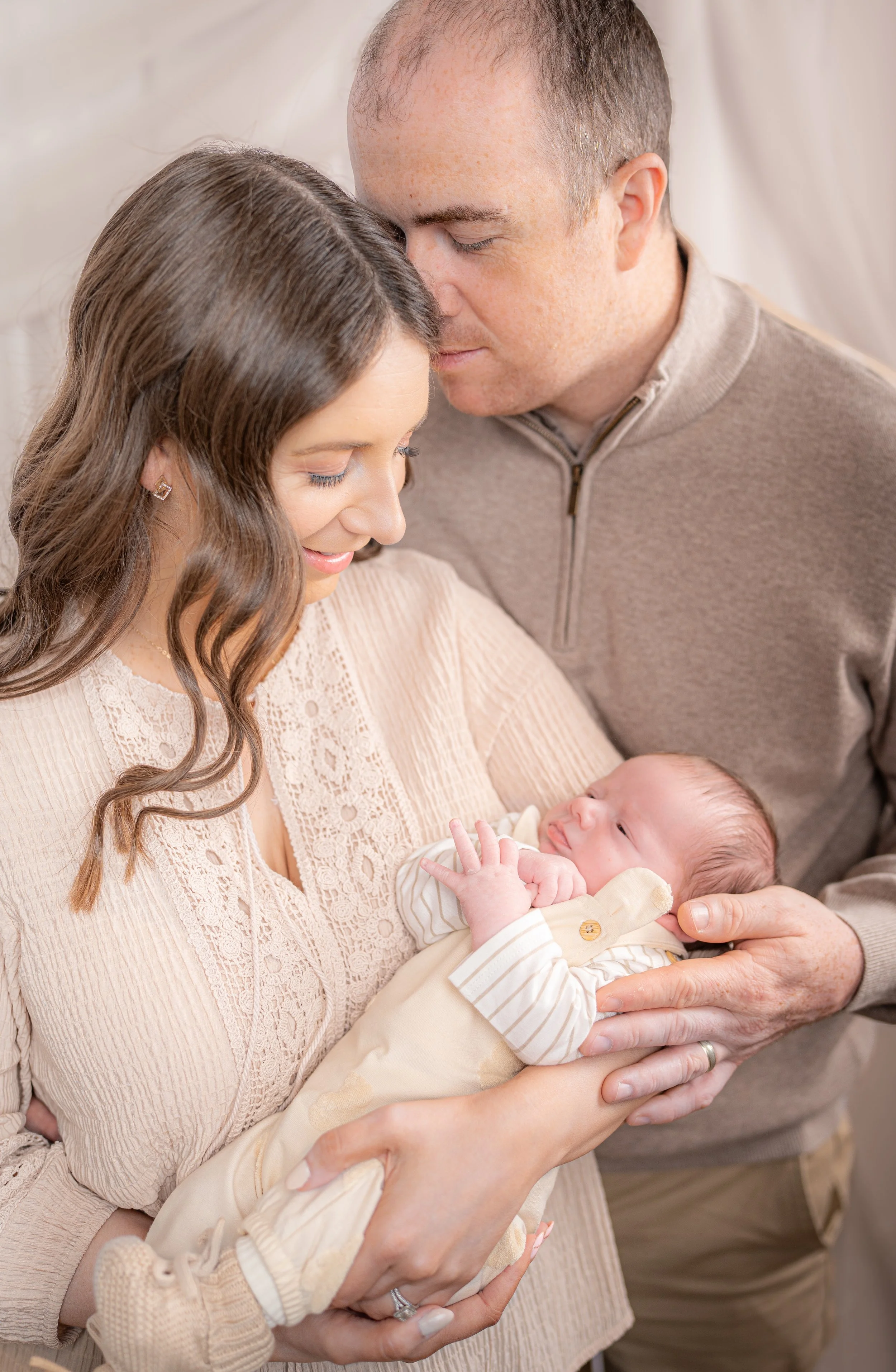 A woman holding a newborn baby, with a man gently touching their foreheads, all sharing a tender moment.