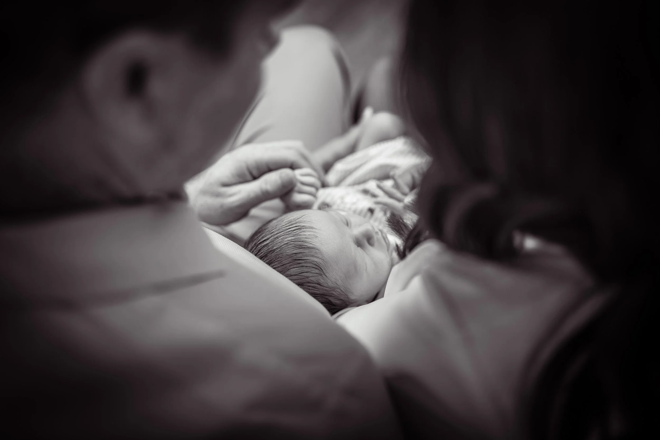 A mother and father holding their newborn baby, who is sleeping, in a close-up black-and-white photo.