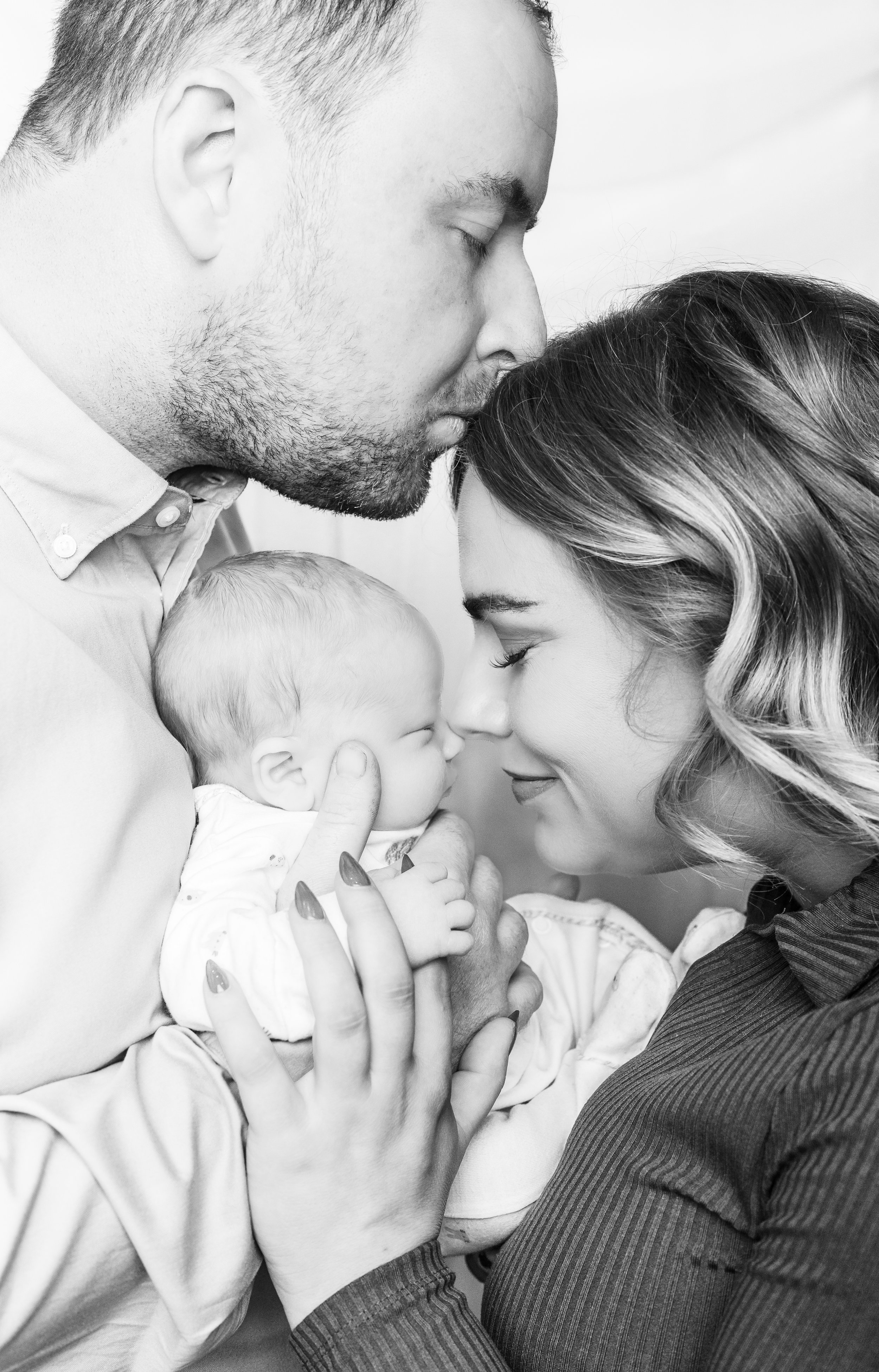 A black and white photo of a family portrait with a man, a woman, and a baby, all with their foreheads touching and eyes closed, expressing love and connection.